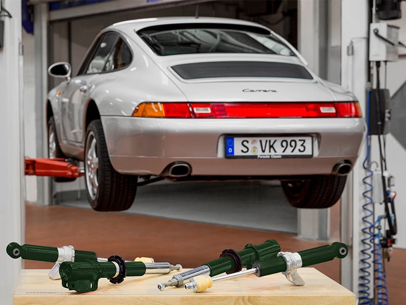 Detail shot: Green shock absorbers for the 993, a Porsche Carrera in the background.