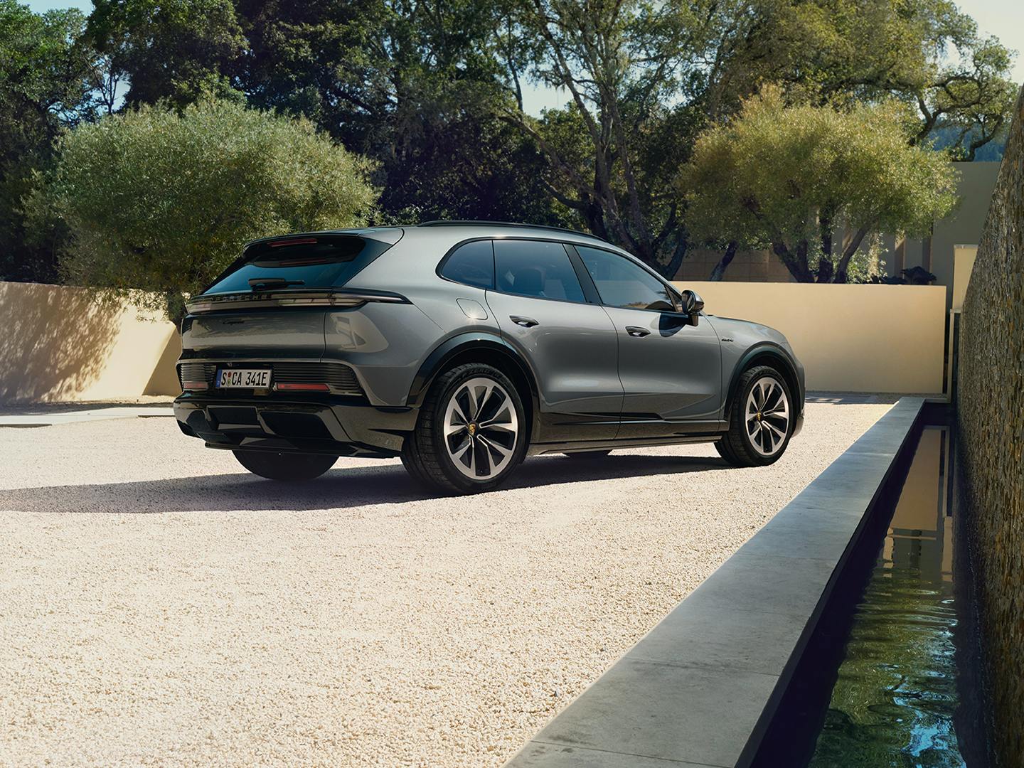 The Cayenne Electric SUV parked on a light coloured pebble ground while facing the wall, there are trees in the background.