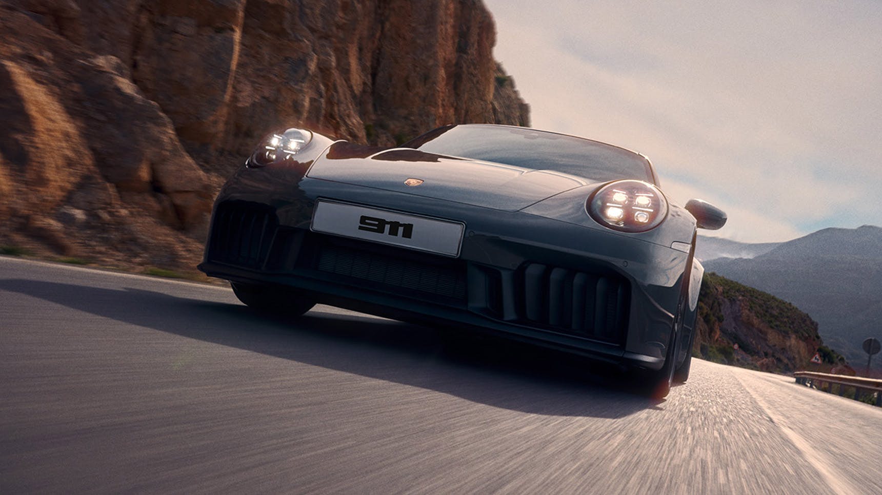 A black Porsche 911 sports car driving on a scenic mountain road, showcasing its sleek design and powerful presence under a clear sky.