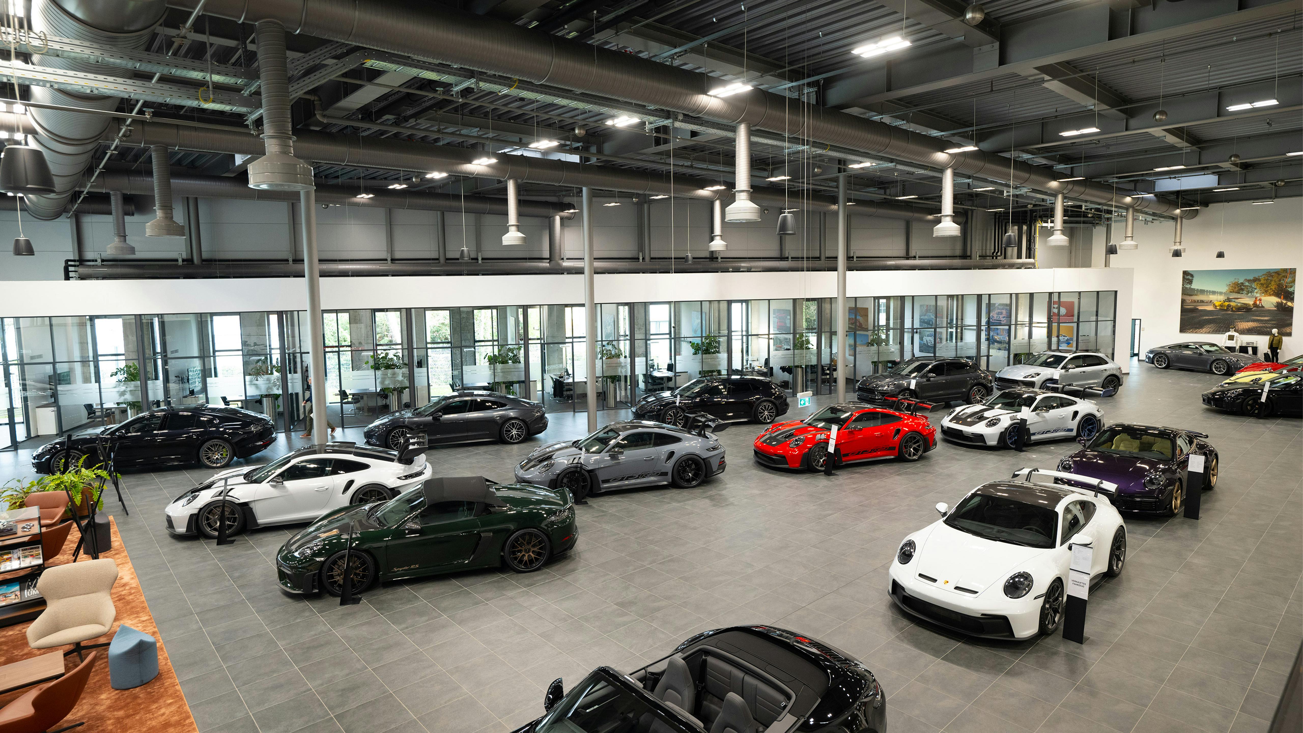 Großer Porsche-Showroom von oben mit schwarzen, weißen, roten und grünen Modellen sowie Sitzbereich.
