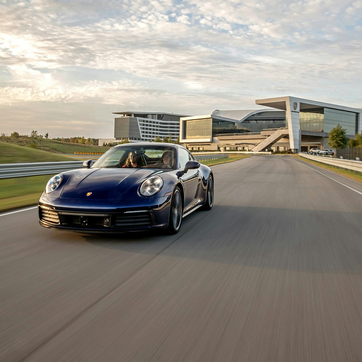 A Porsche car in movement on a track with a Porsche Experience Center building in the background.