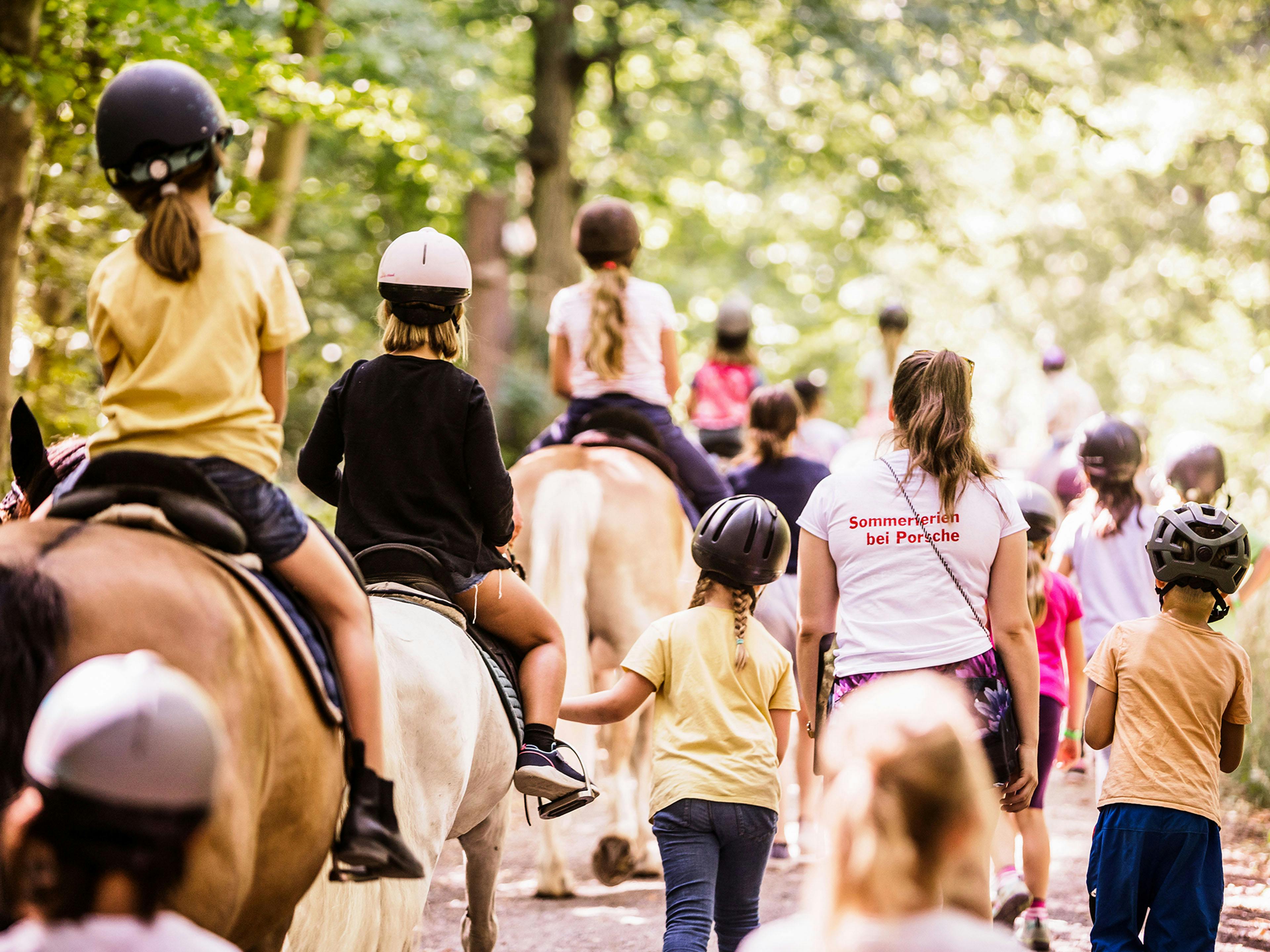 Mehrere behelmte Kinder auf Pferden von hinten.