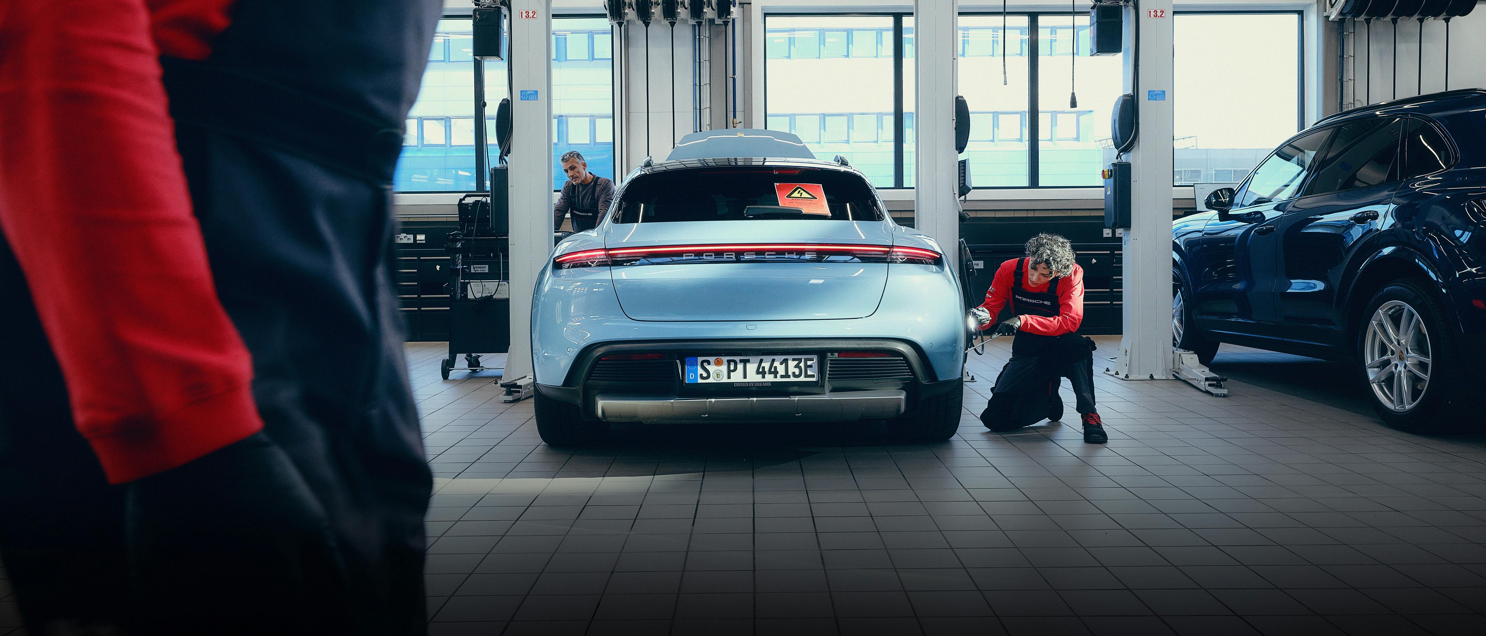 Ein Porsche Taycan wird in der Werkstatt von Porsche-Mitarbeitern inspiziert