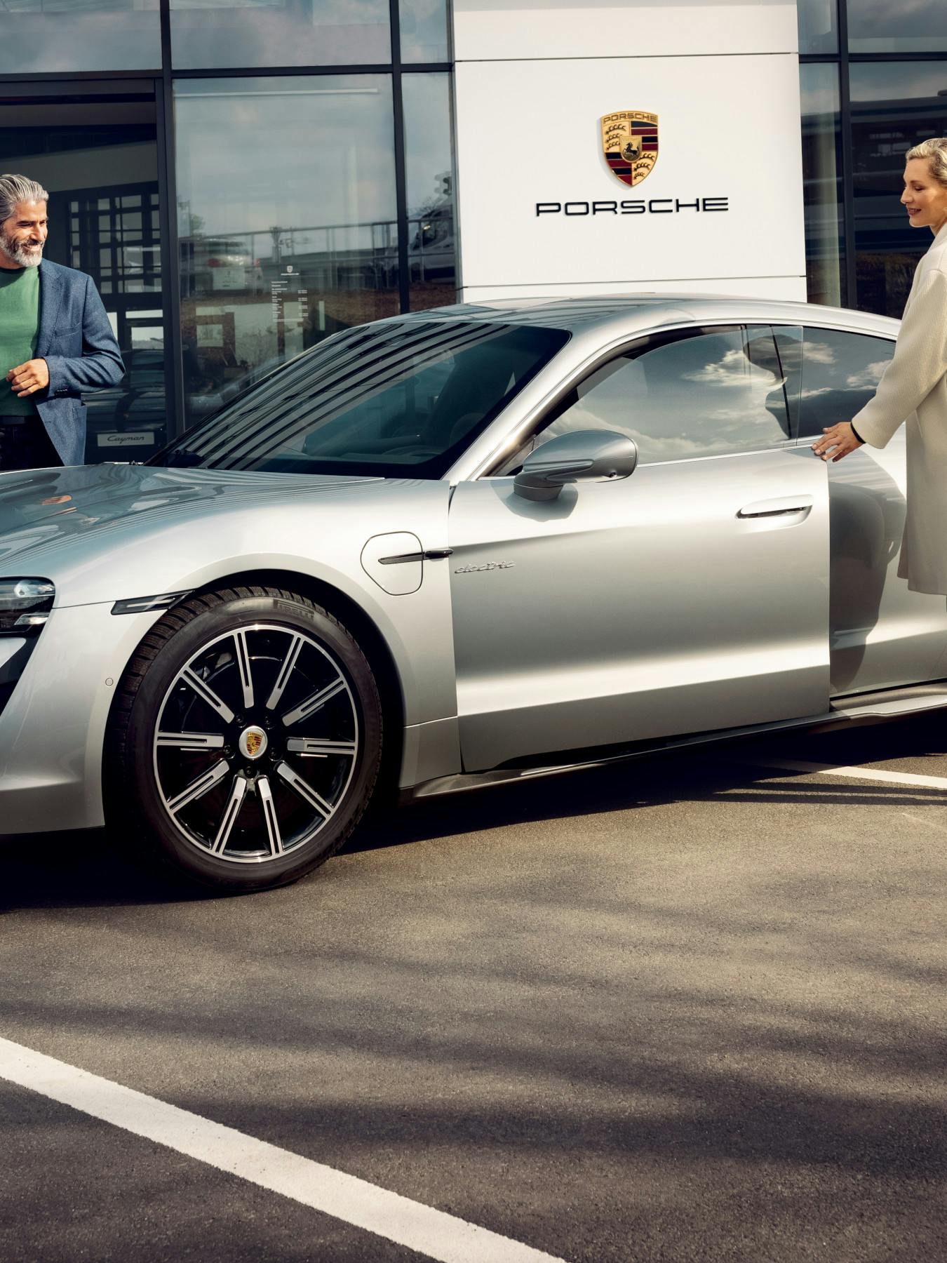 A family standing next to a silver Taycan in front of a Porsche Centre.