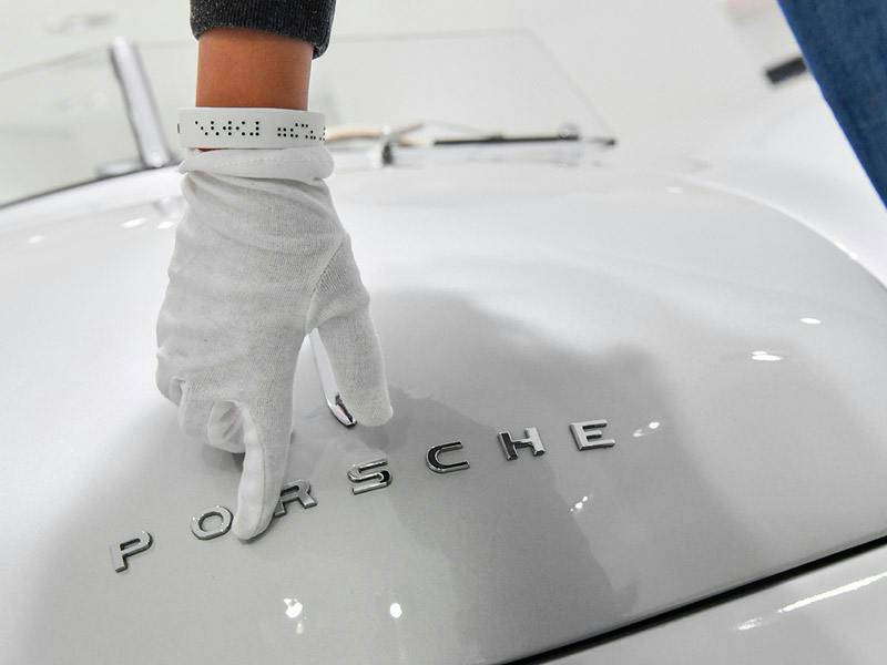 A person running a gloved hand over a white Porsche in a guided tour for visually impaired visitors of the Porsche Museum