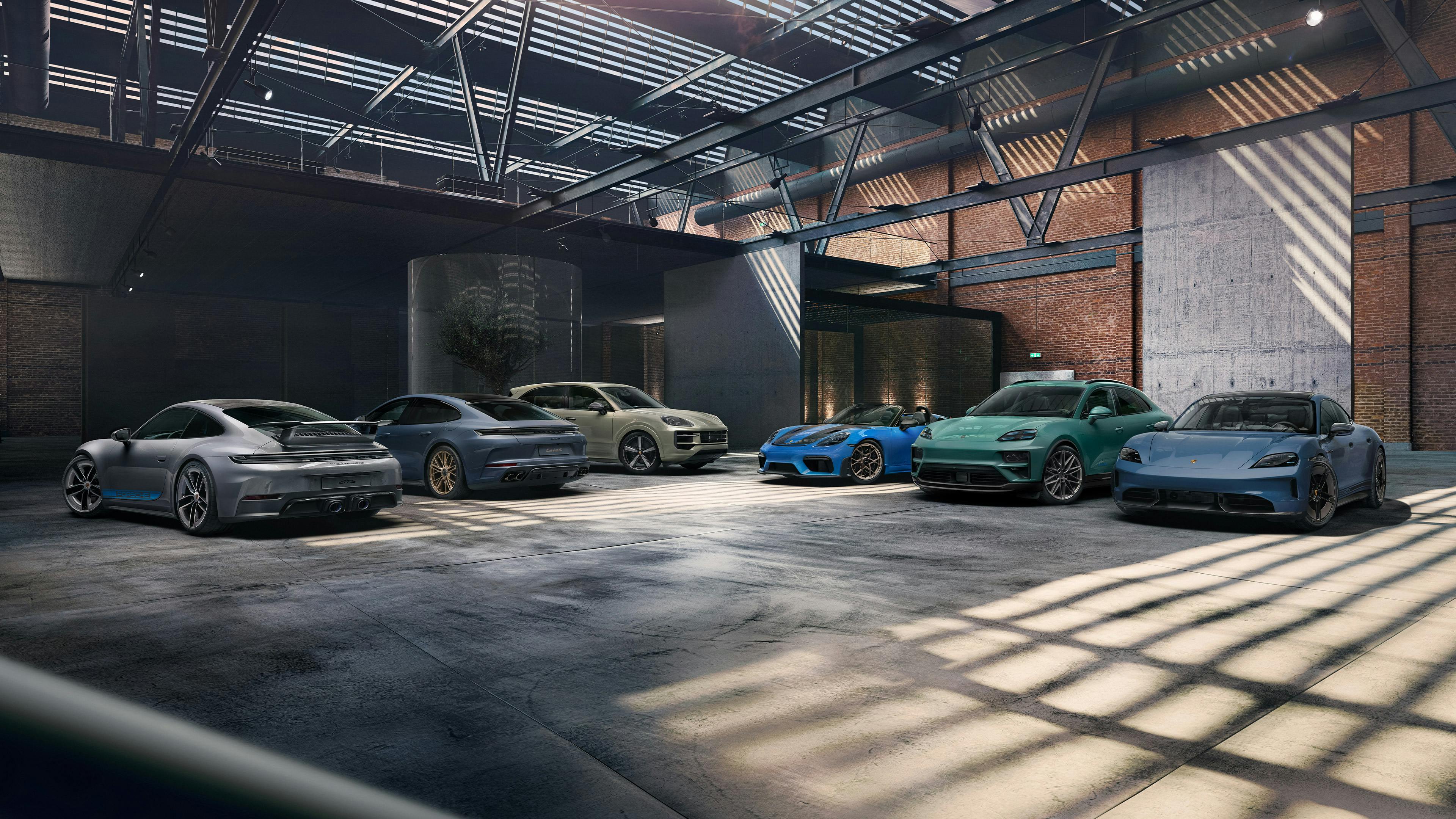 Sechs unterschiedliche Sportwagen stehen nebeneinander in einer grossen Halle mit Backsteinwänden, Stahlträgern und natürlichem Lichteinfall.