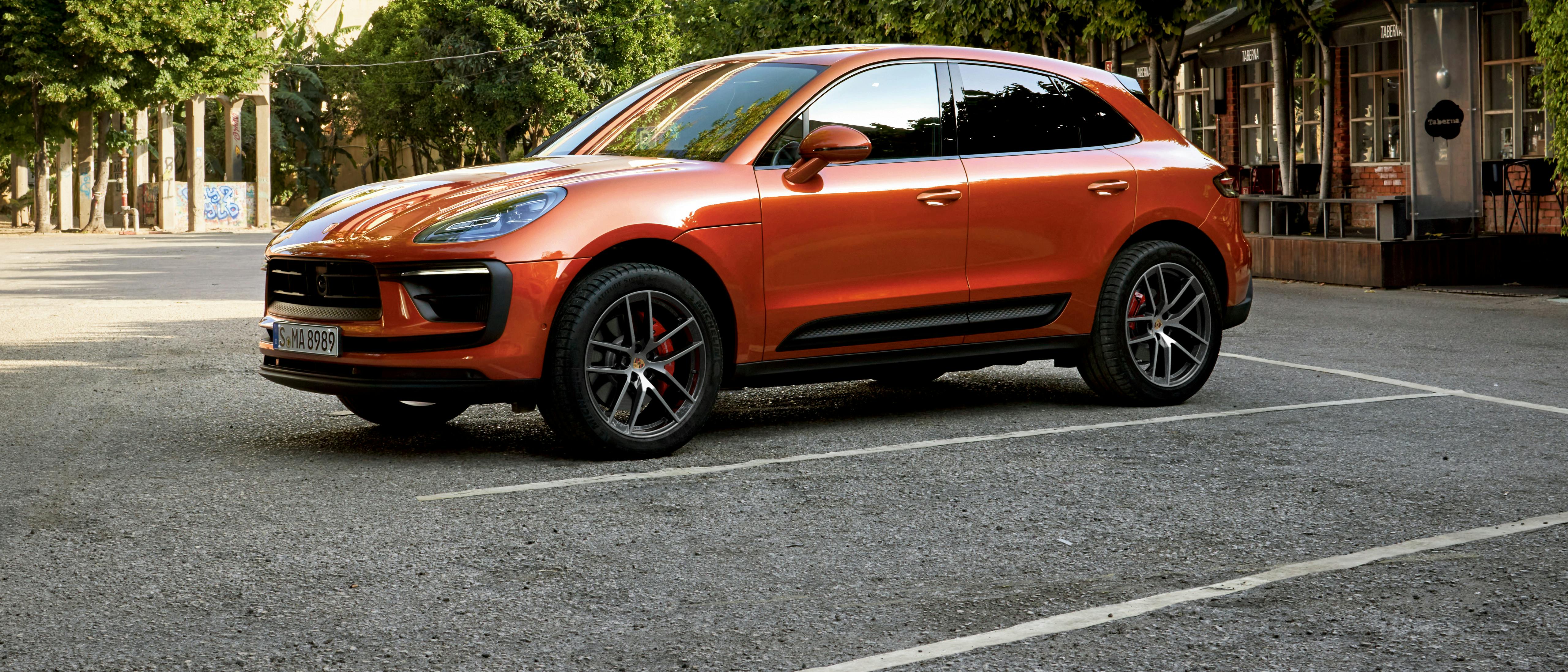 The Macan S in white lined parking bay, with trees and building visible in the background.