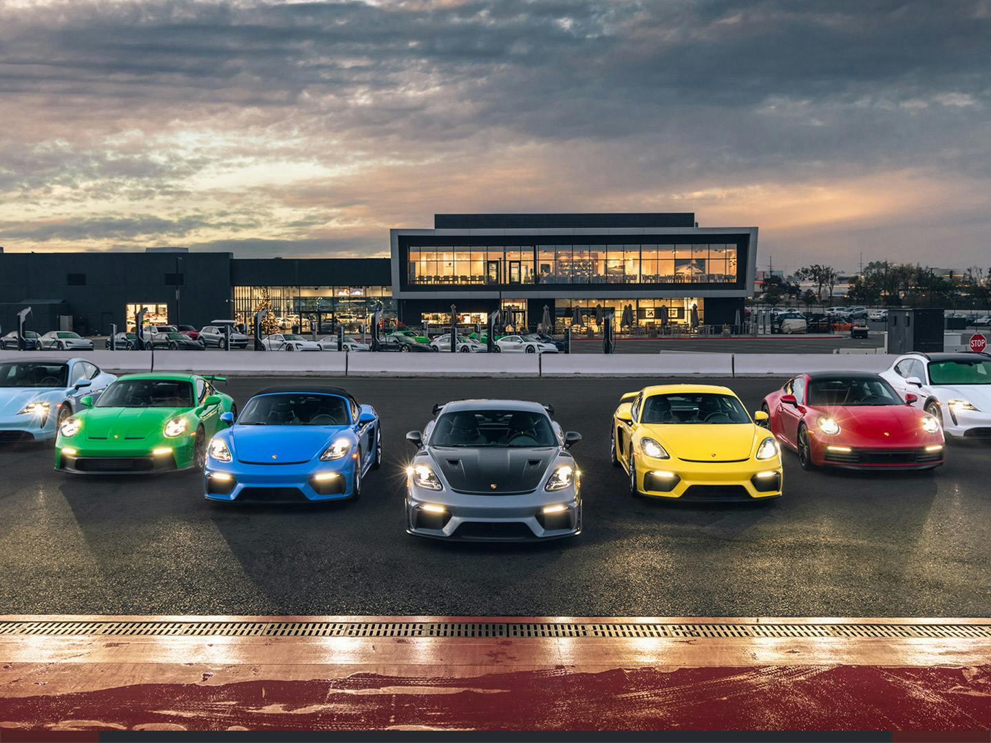 Siete vehiculos Porsche alineados al anochecer frente al Porsche Experience Center de Los Ángeles.