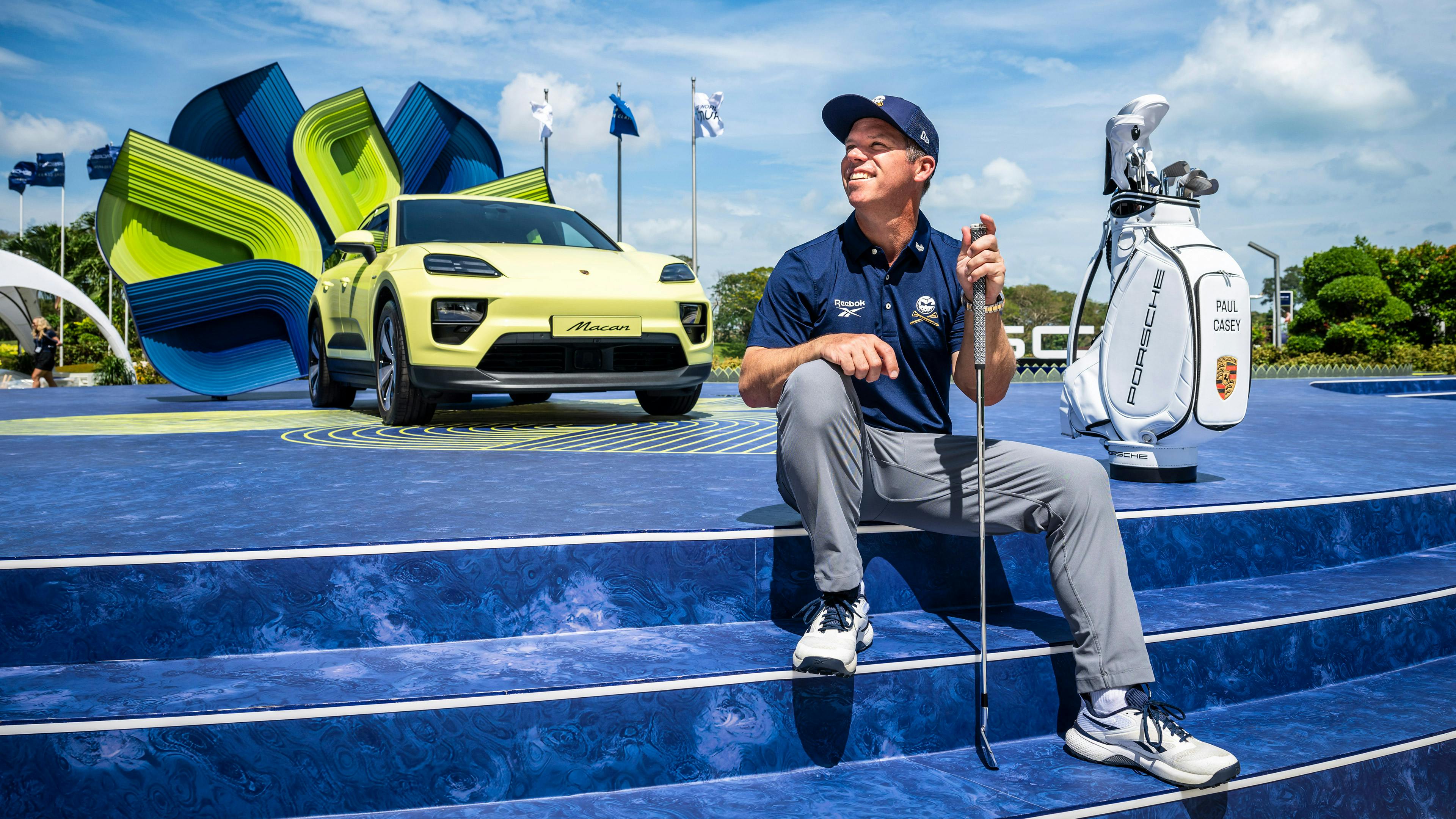 Golfer Paul Casey beim Porsche Golf-Event in Singapur mit gelbem Porsche Macan im Hintergrund.