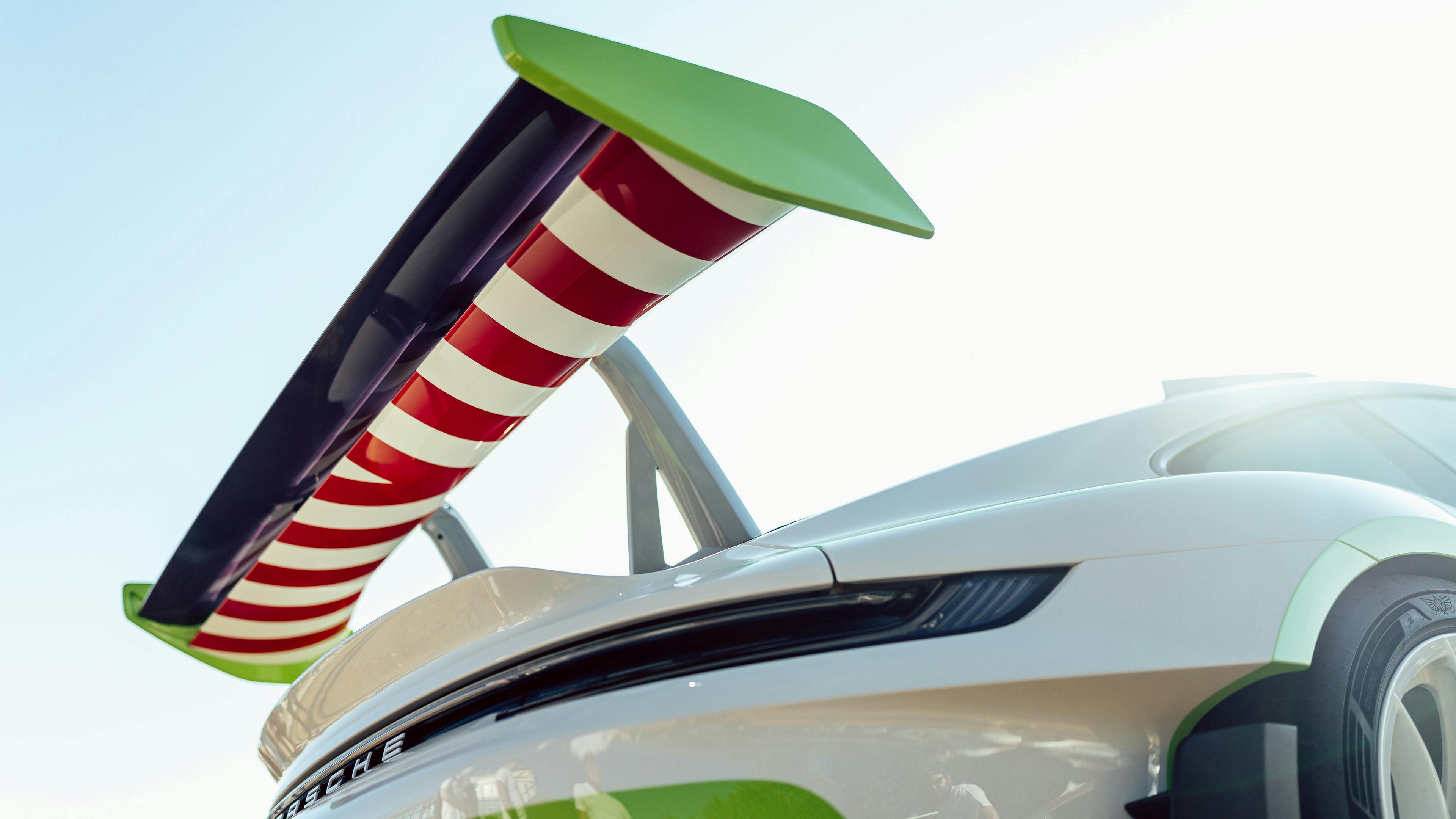 Rear wing detail of the Buzz Lightyear-inspired Porsche 911 GT3 RS, showing the white and Fire Red striped lower wing element against the car's green and white bodywork.