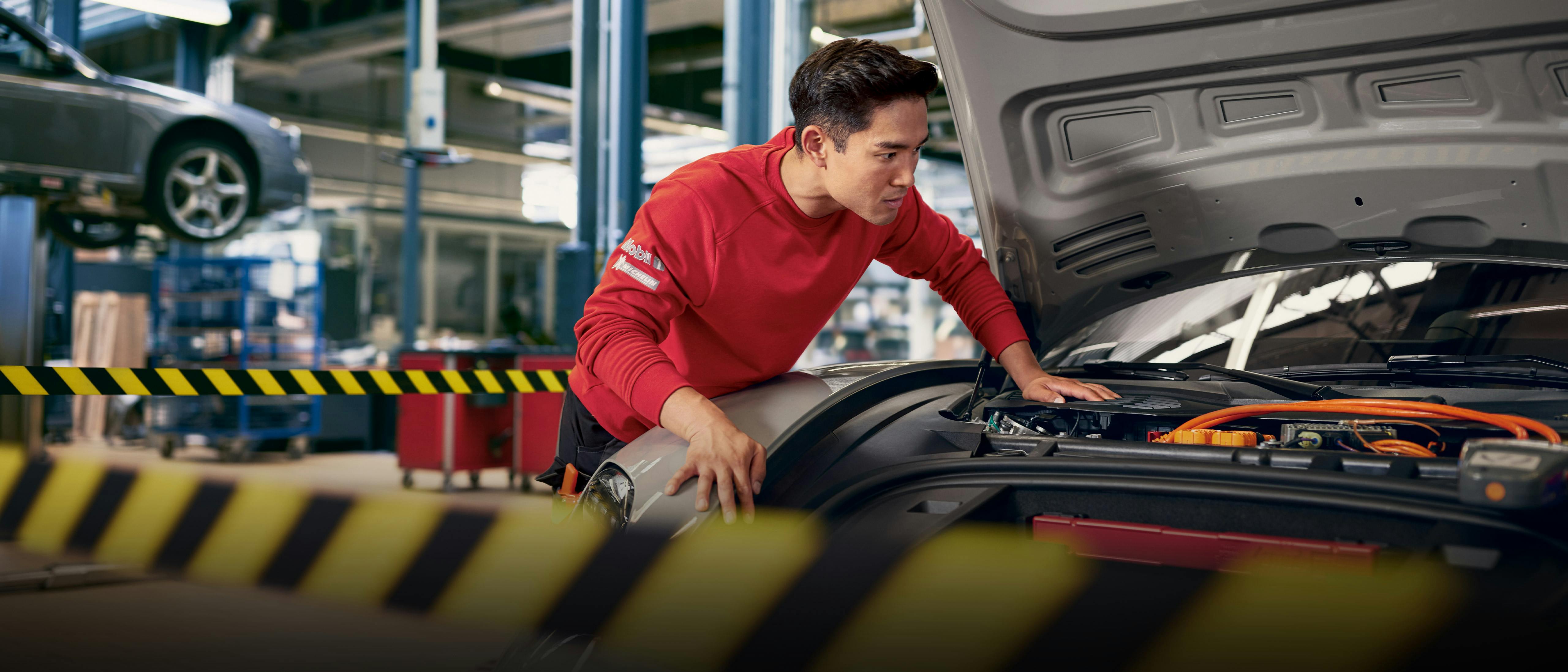 A workshop employee looks under the open bonnet of a Porsche Taycan.