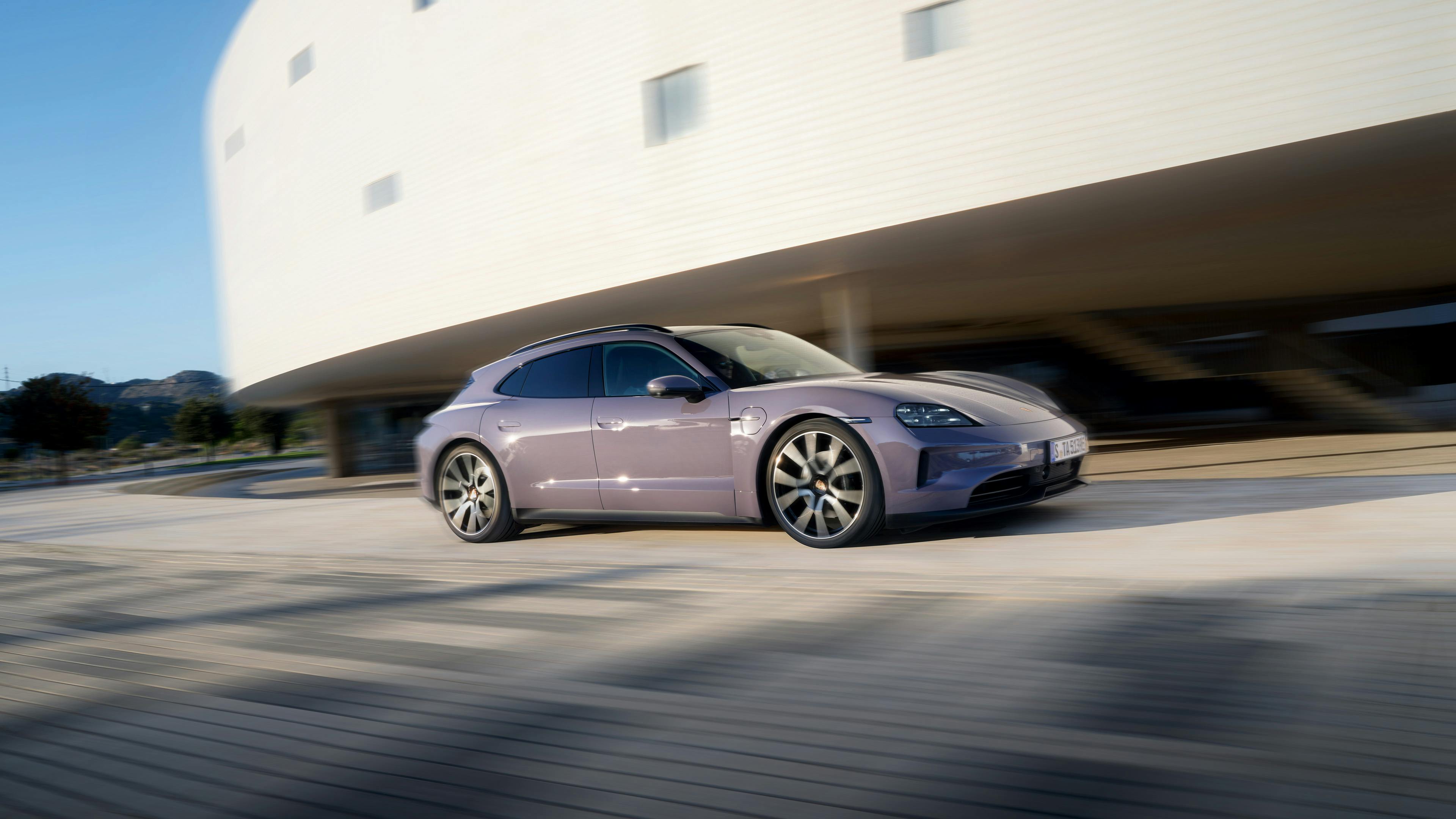 Een Porsche Taycan Sport Turismo rijdt langs een groot wit gebouw.