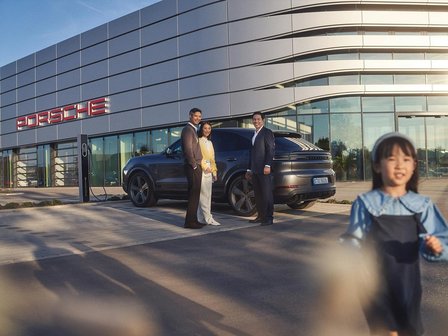 A couple and a Porsche consultant having a conversation in front of a Porsche Centre.
