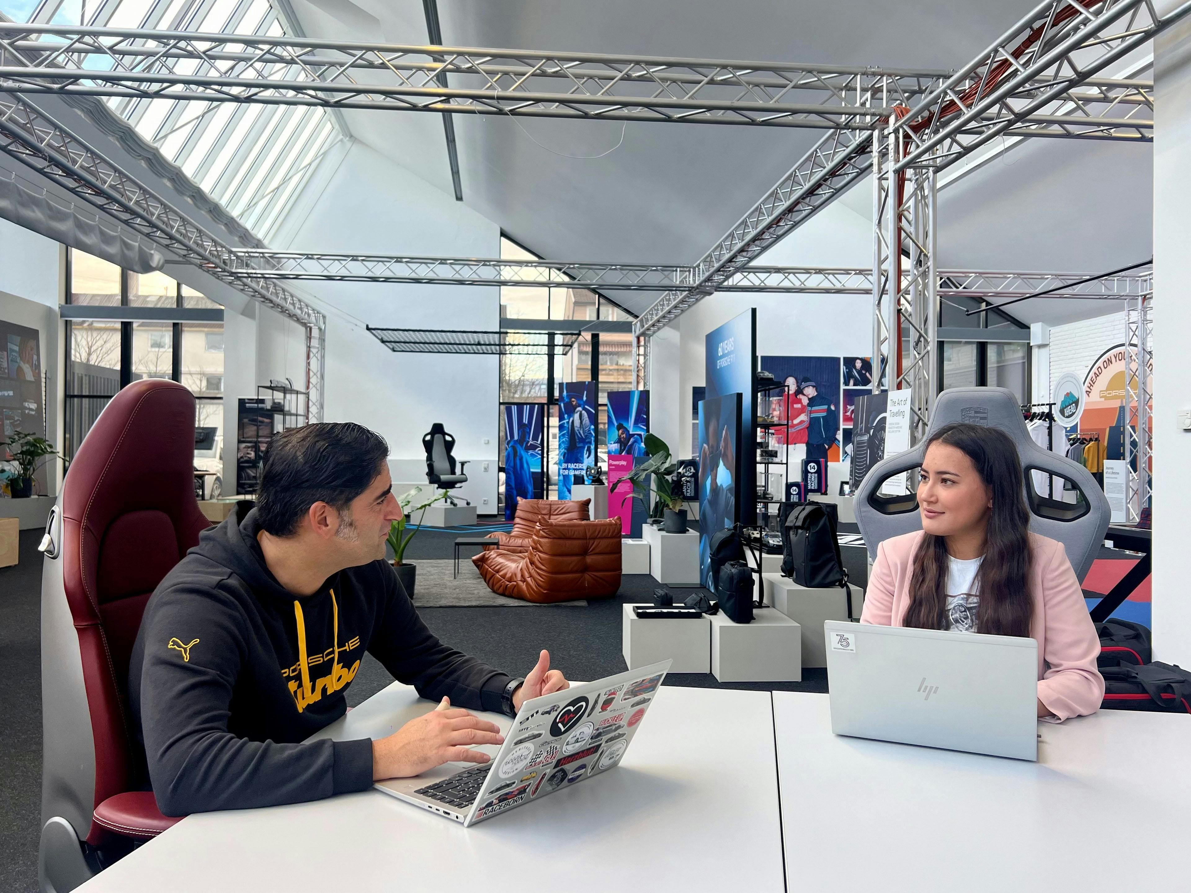 Schwarz-Weiß-Aufnahme: Porsche Mitarbeiterinnen und Mitarbeiter sitzen gemeinsam mit Laptops an einem grossen Tisch.