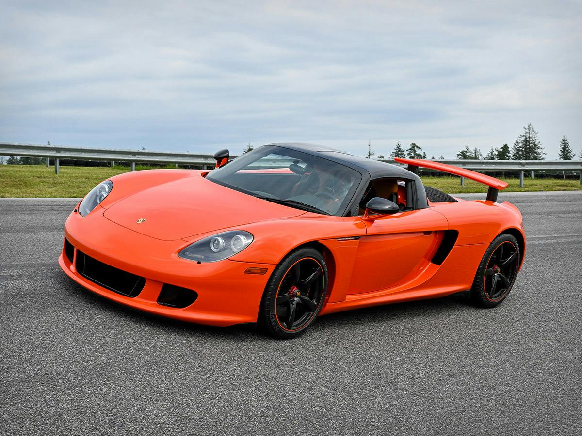 Front and side top‑down view of the Carrera GT in Continentalorange, photographed slightly tilted downward onto the racetrack.