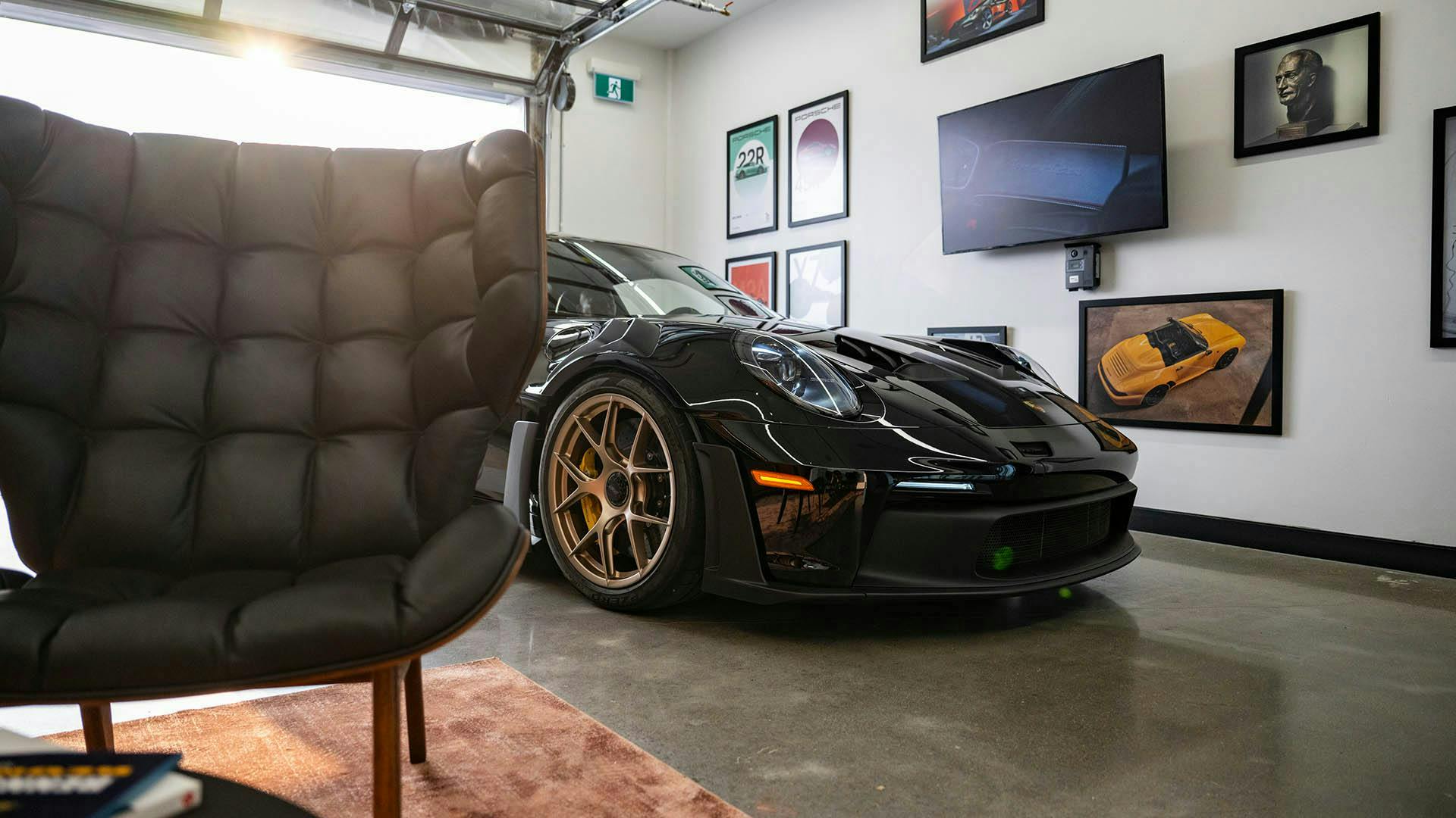 A black Porsche 911 GT3 RS in a lounge, partially obscured by a lounge chair. ​