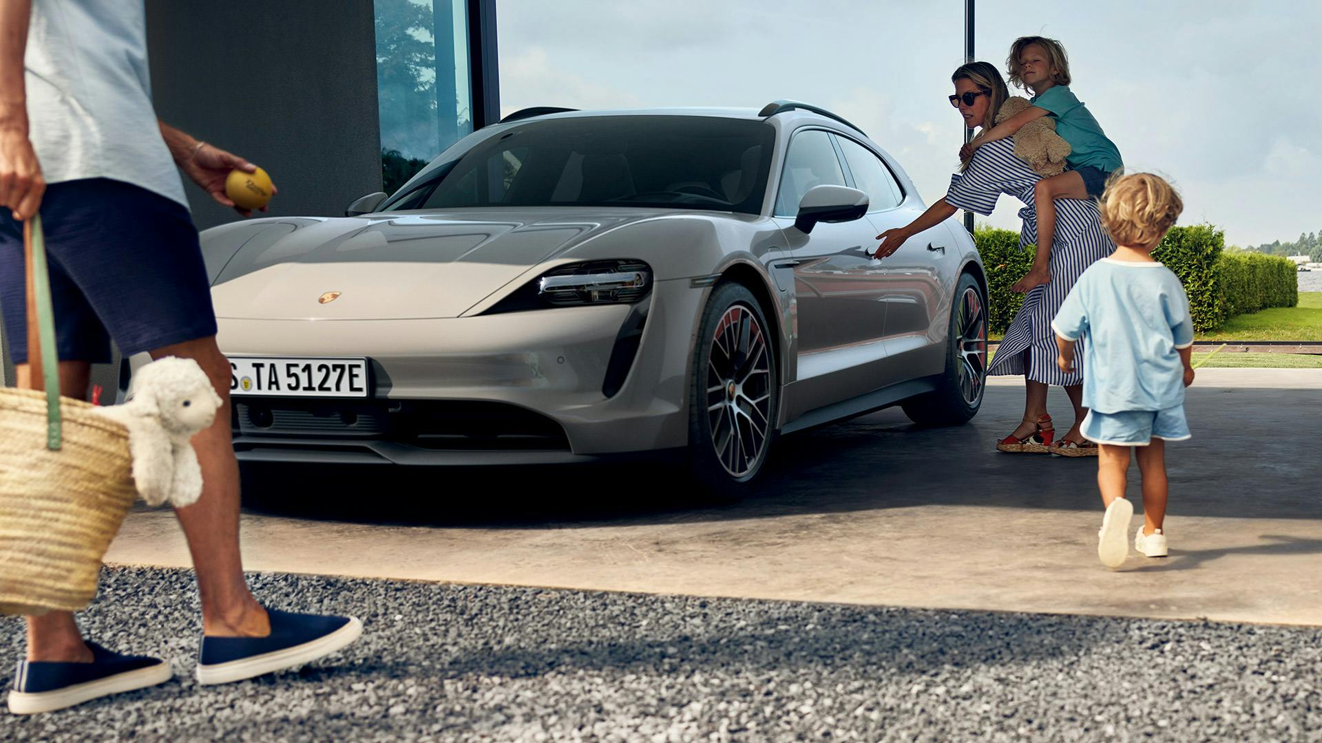 Una madre con un niño a cuestas abre la puerta delantera del Porsche Taycan.