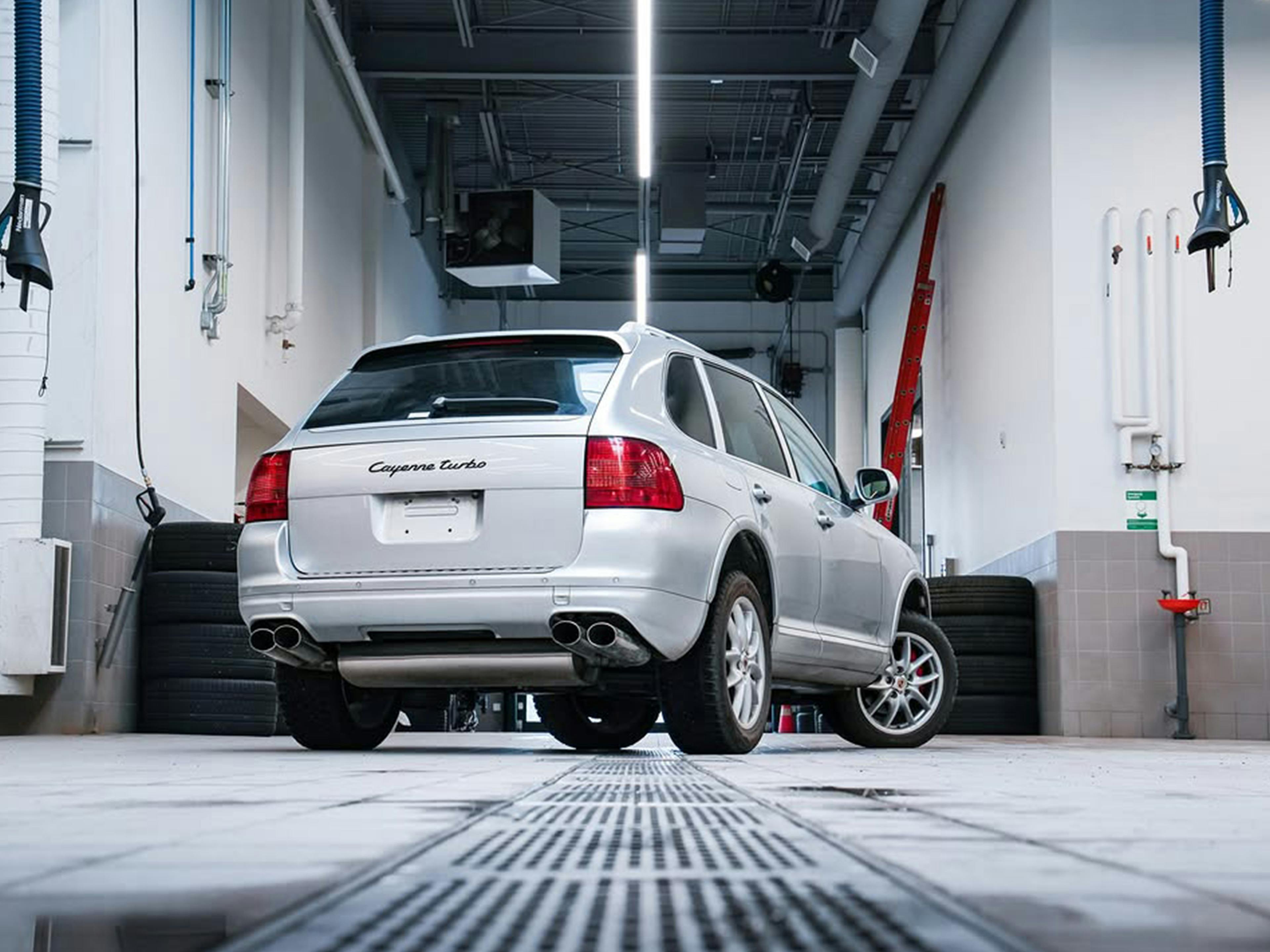 A rear shot of a silver first-generation Porsche Cayenne in a clean, brightly-lit service bay.