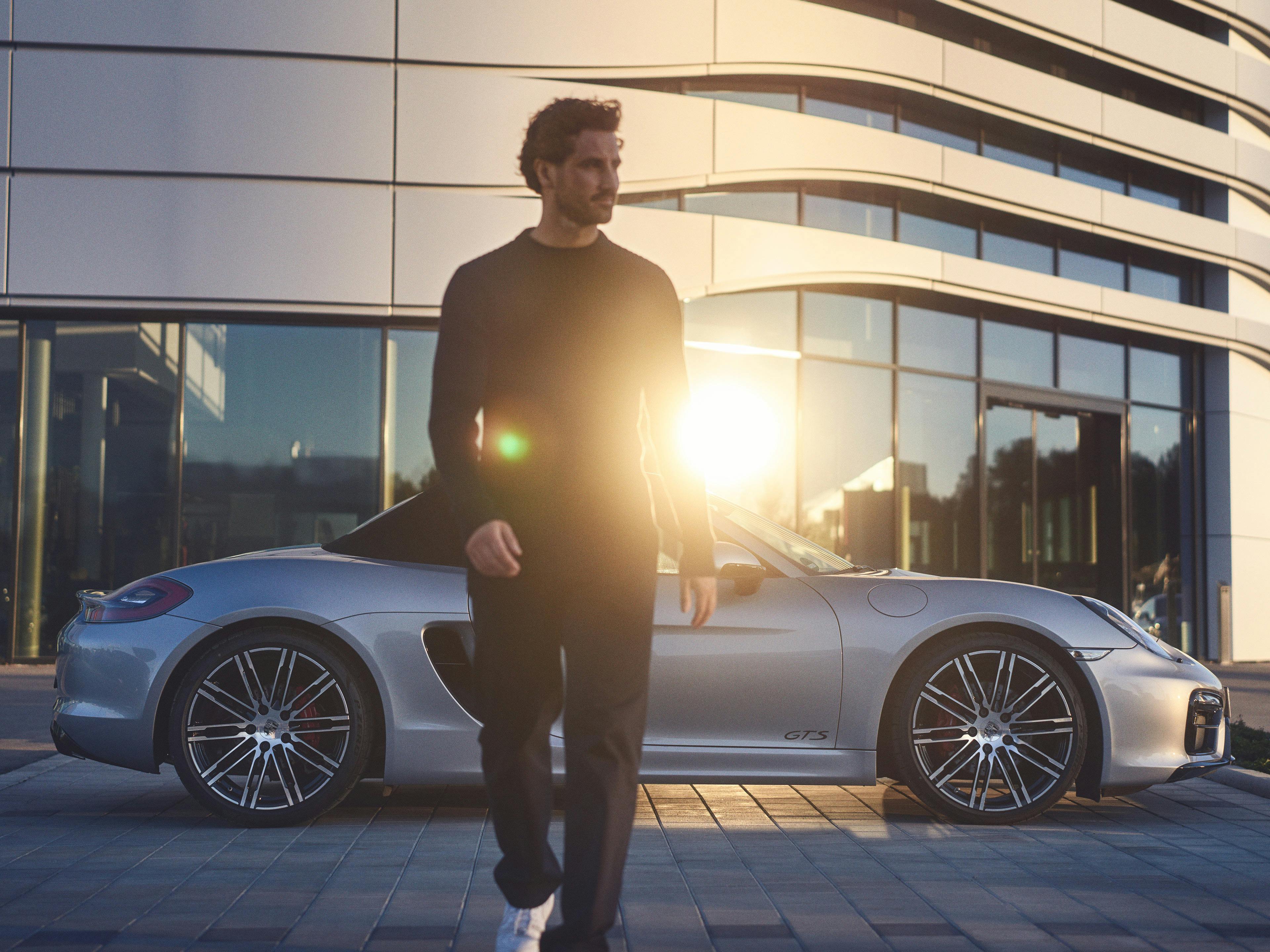 A man walking away from a Porsche 718 GTS that is parked outside a Porsche Centre.