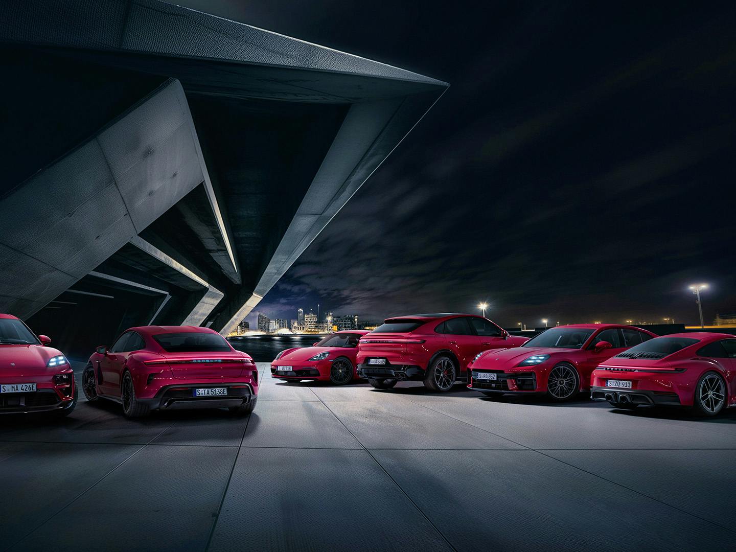 All Porsche models parked outside a dark building, the cars are in Carmine Red.