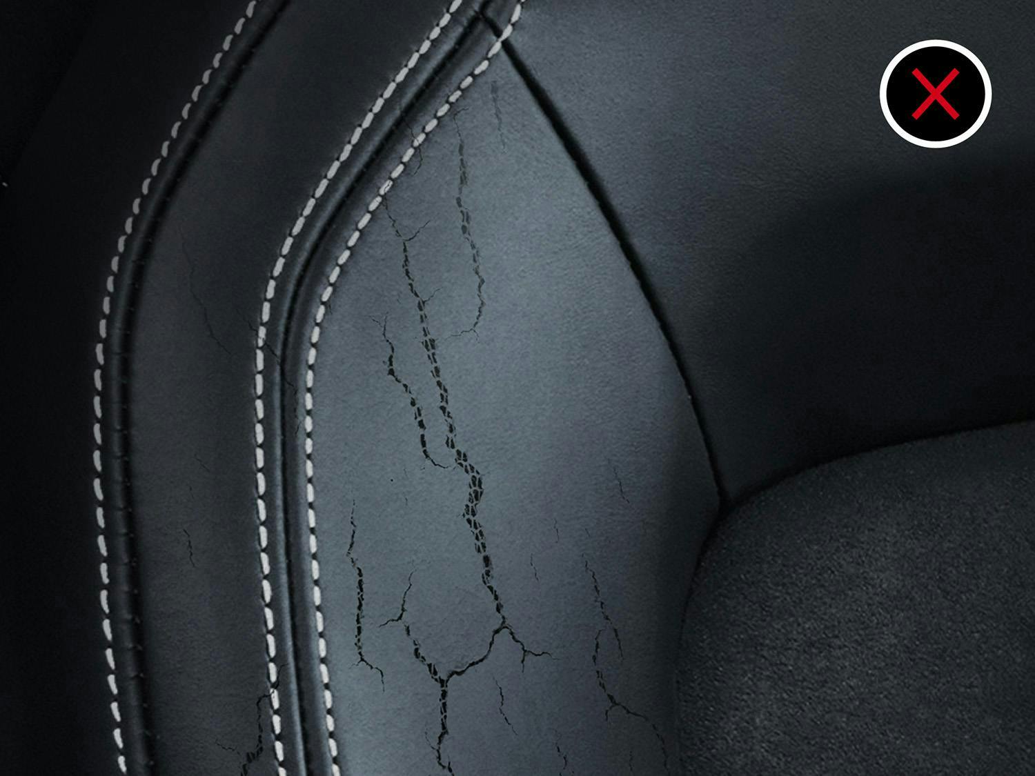 Close-up of a black car seat with cracked and damaged leather, marked with a cross symbol.
