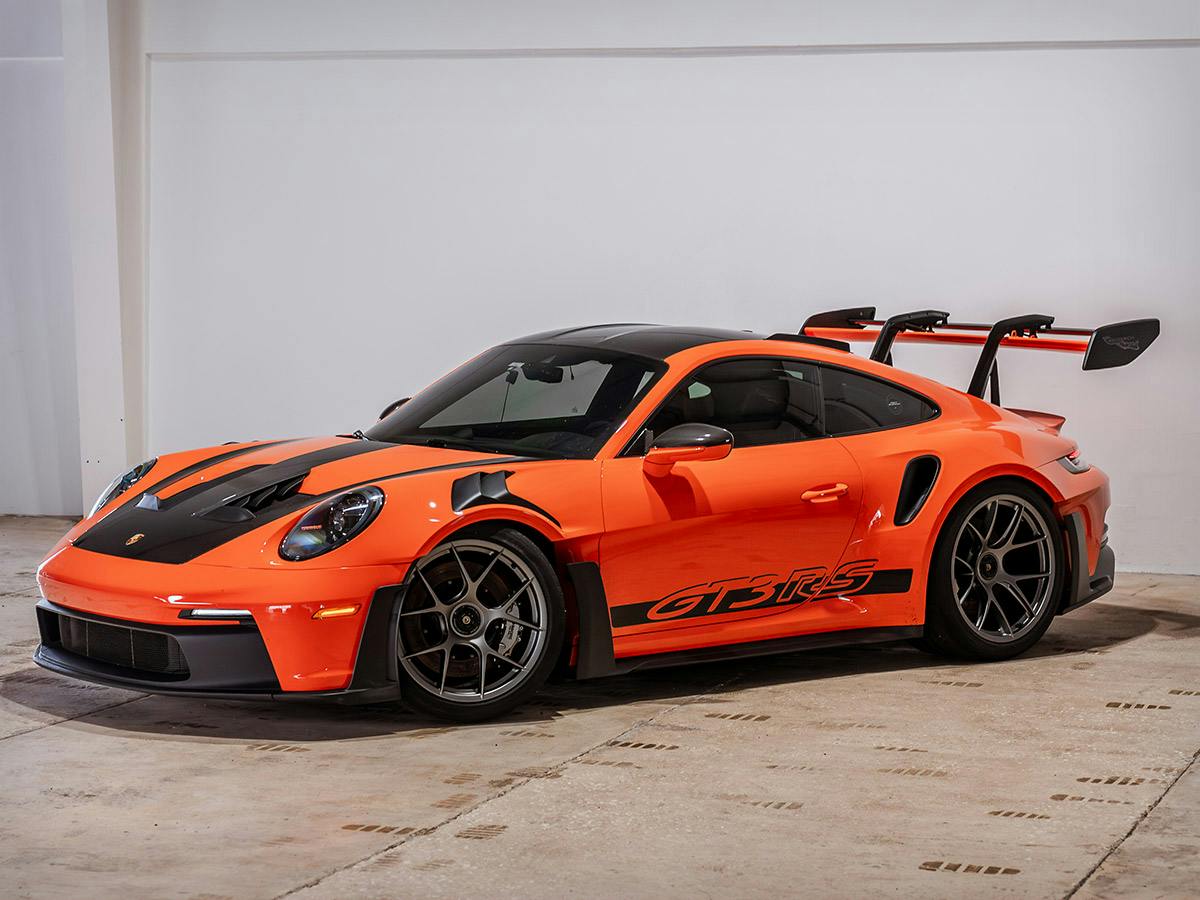 991 GT3 RS in Paint to Sample colour Gulforange with black accents and orange GT3 RS side decals, parked indoors on a concrete floor.