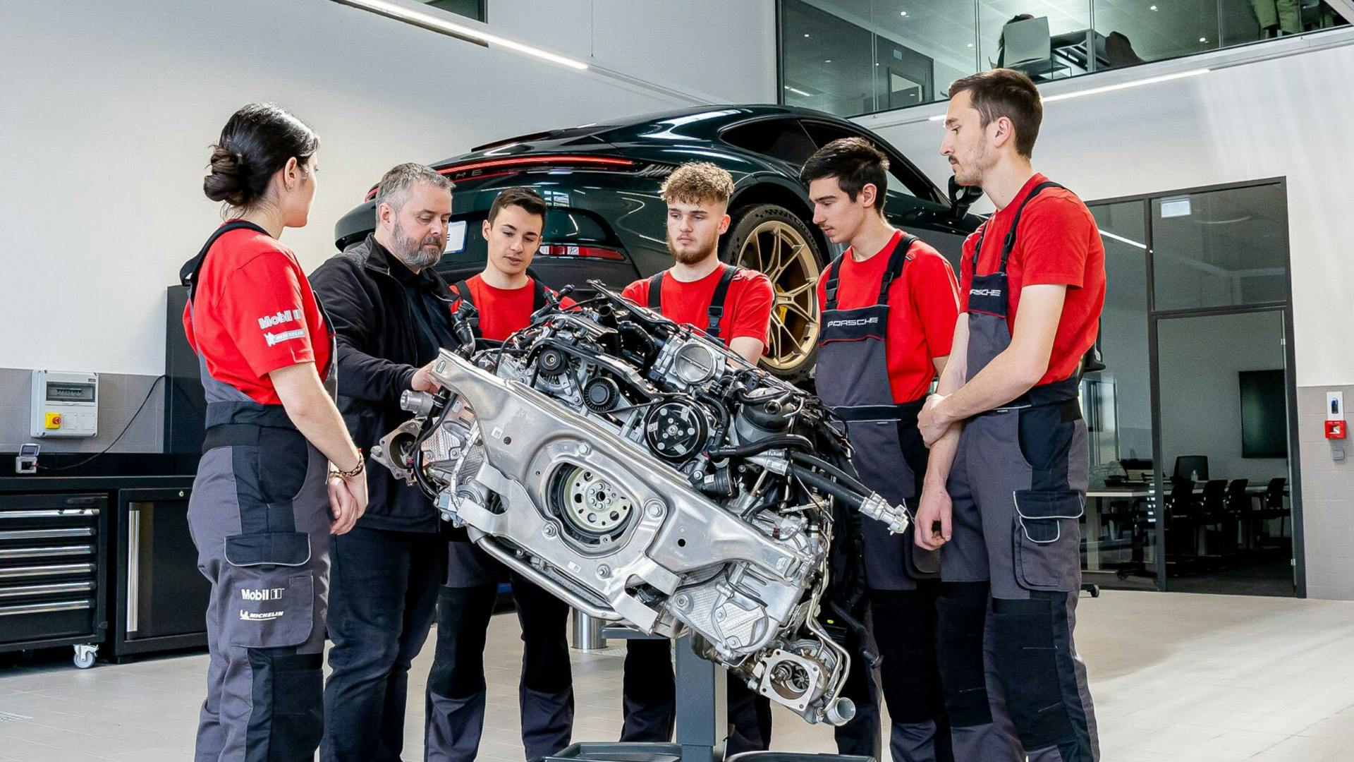 Un formateur du Porsche Institut forme cinq élèves sur un bloc moteur