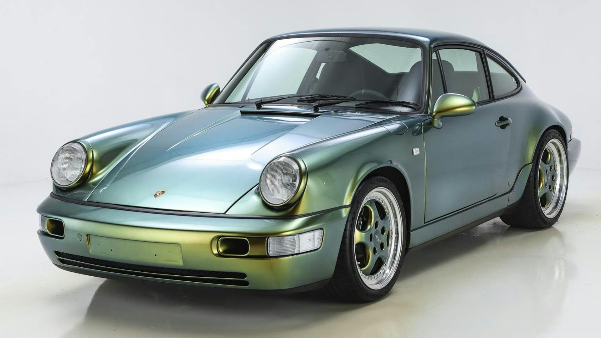 A classic 911 sports car with an iridescent blue-green paint glistens in a well-lit studio.