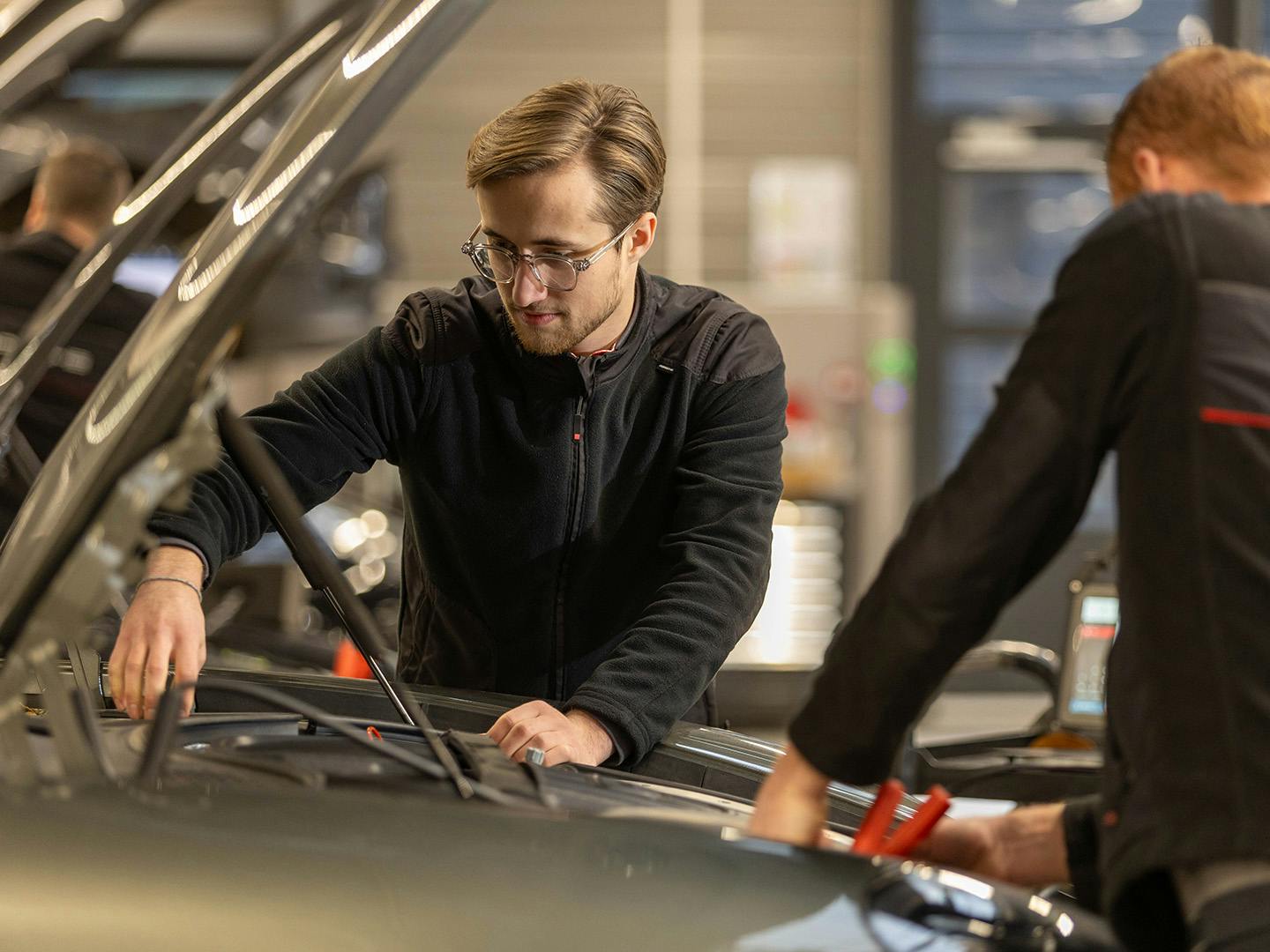 Deux techniciens Porsche travaillent sous le capot d'un véhicule Porsche.