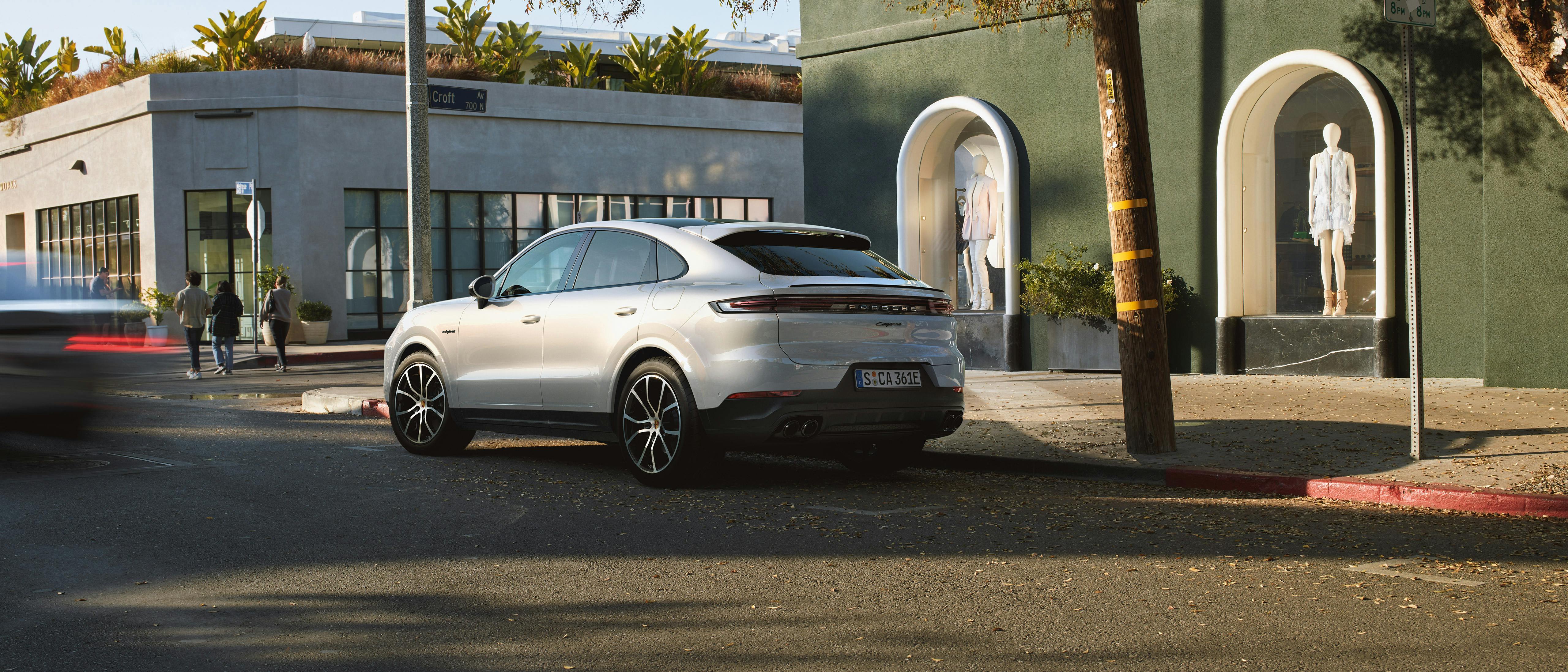 Un Porsche Cayenne E-Hybrid garé devant une boutique.