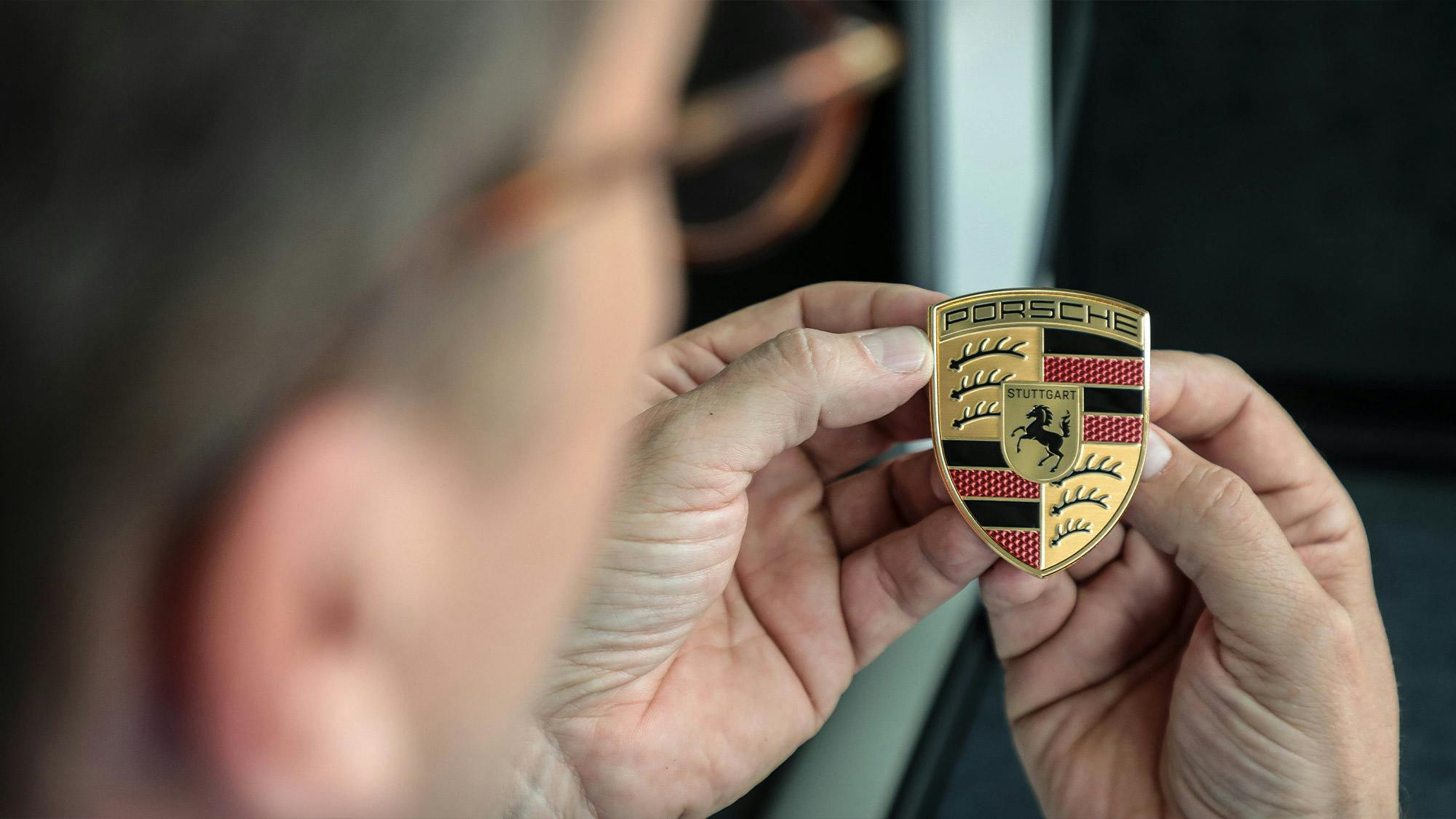 Un uomo guarda l'iconico scudo Porsche che ha tra le mani.