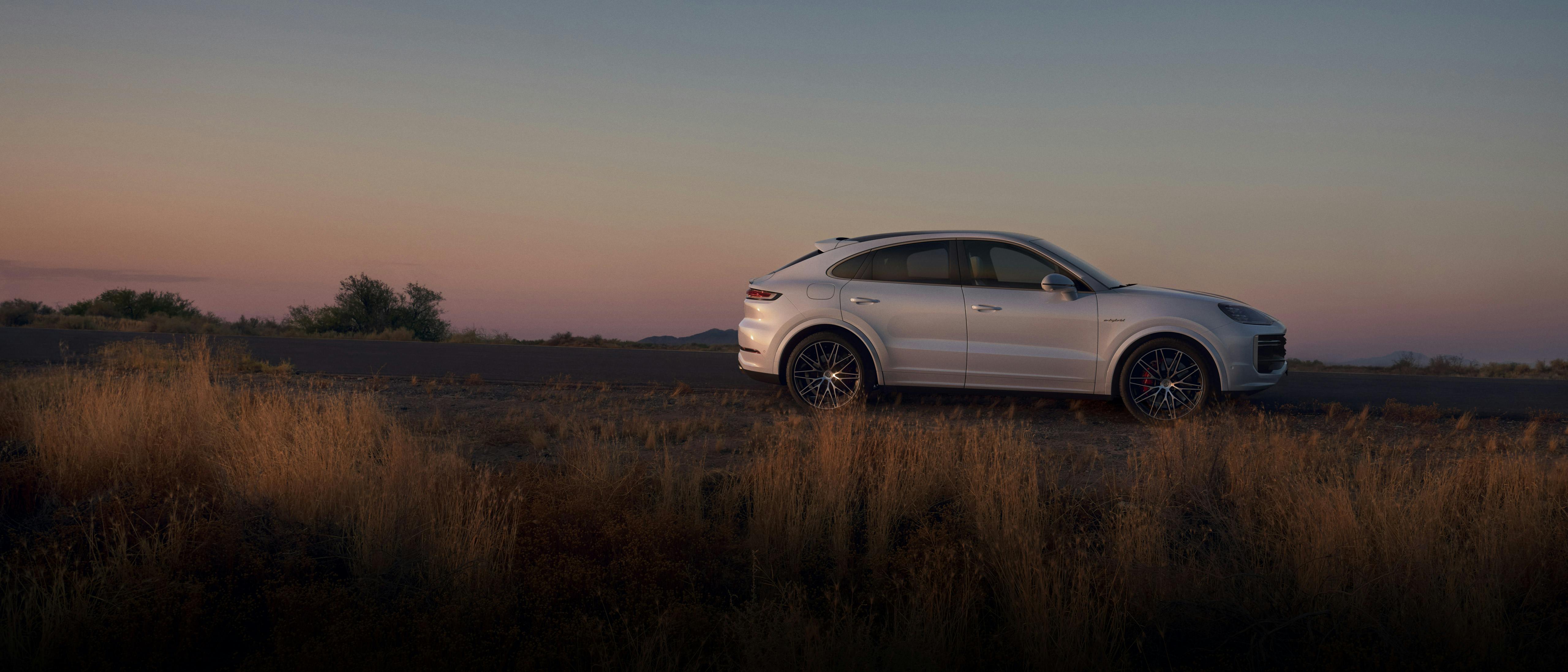 Weißer Porsche Cayenne steht seitlich auf einer Straße in einer trockenen Landschaft mit hohem Gras.