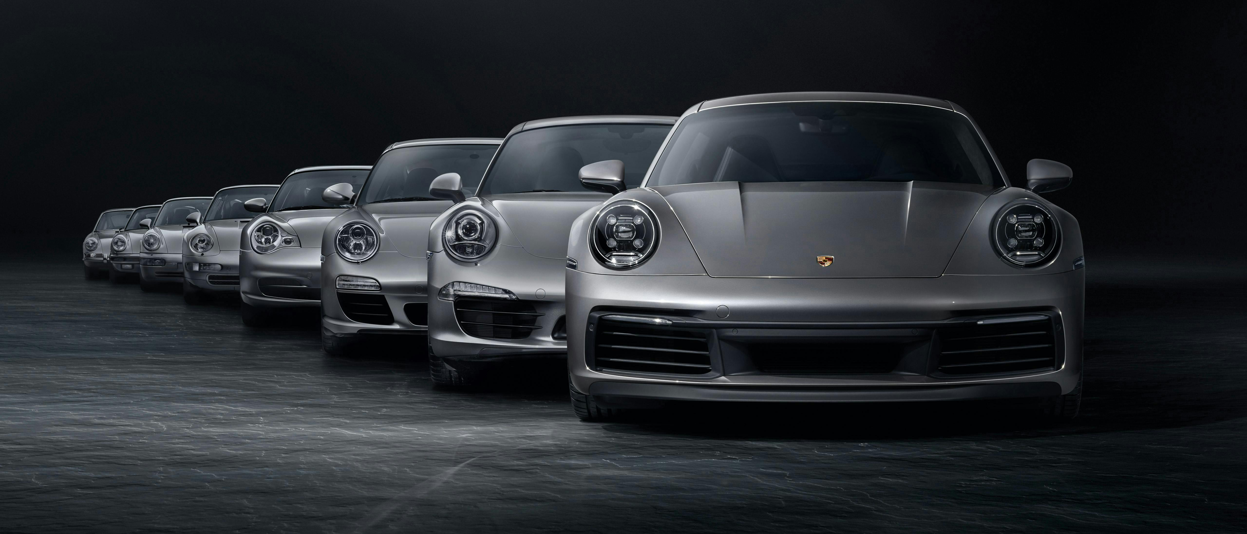 In a black studio, various silver Porsche 911 generation models are lined up in a row.