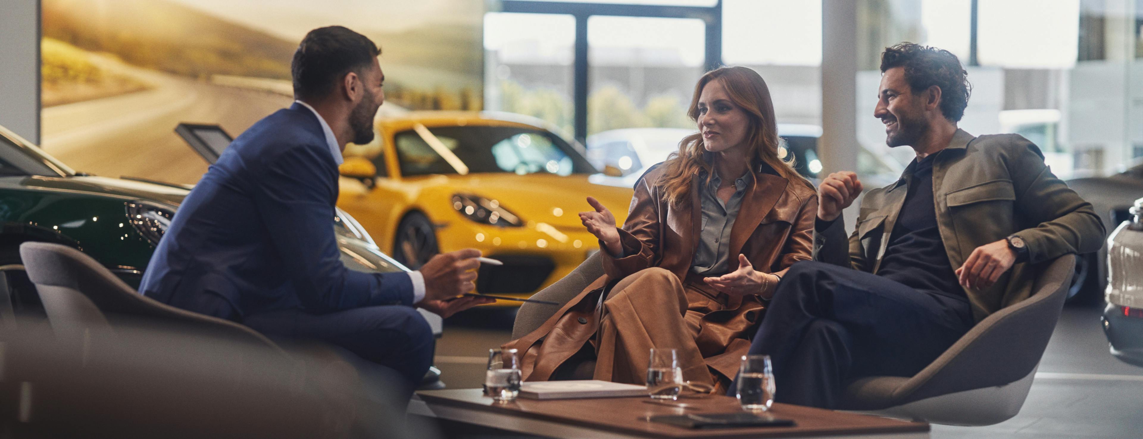 A Porsche service employee is speaking to two customers in an Authorized Porsche Center in a pleasant atmosphere.