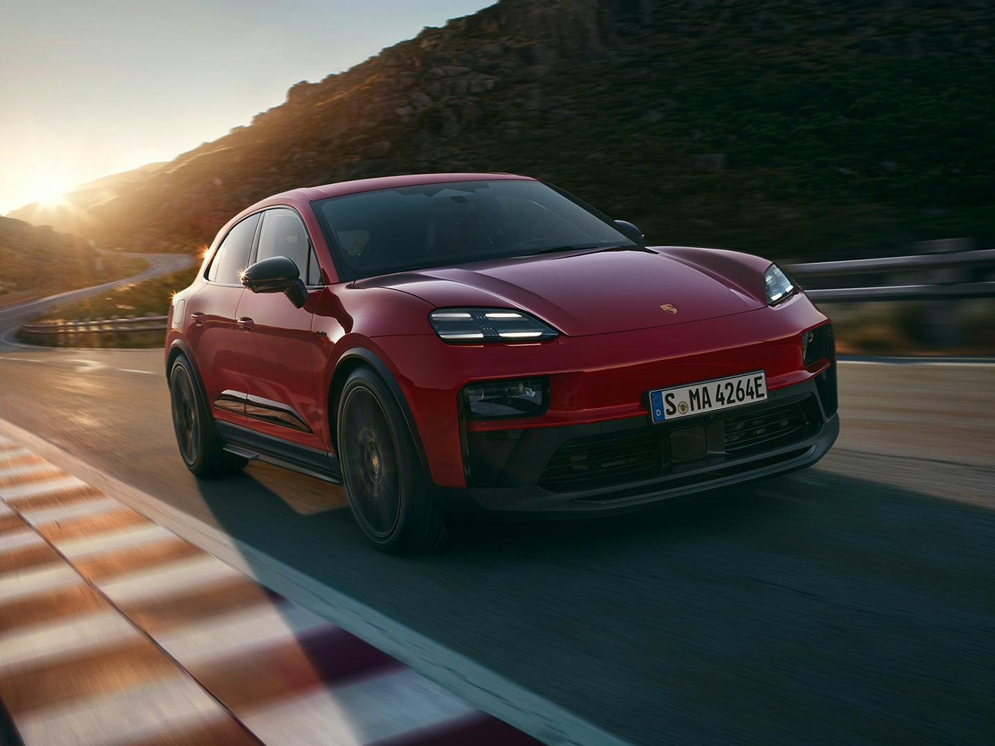 Εμπρόσθια τριών τετάρτων όψη της νέας Macan GTS, εν κινήσει σε κόκκινη απόχρωση, σε κατάσταση ηλιοβασιλέματος.