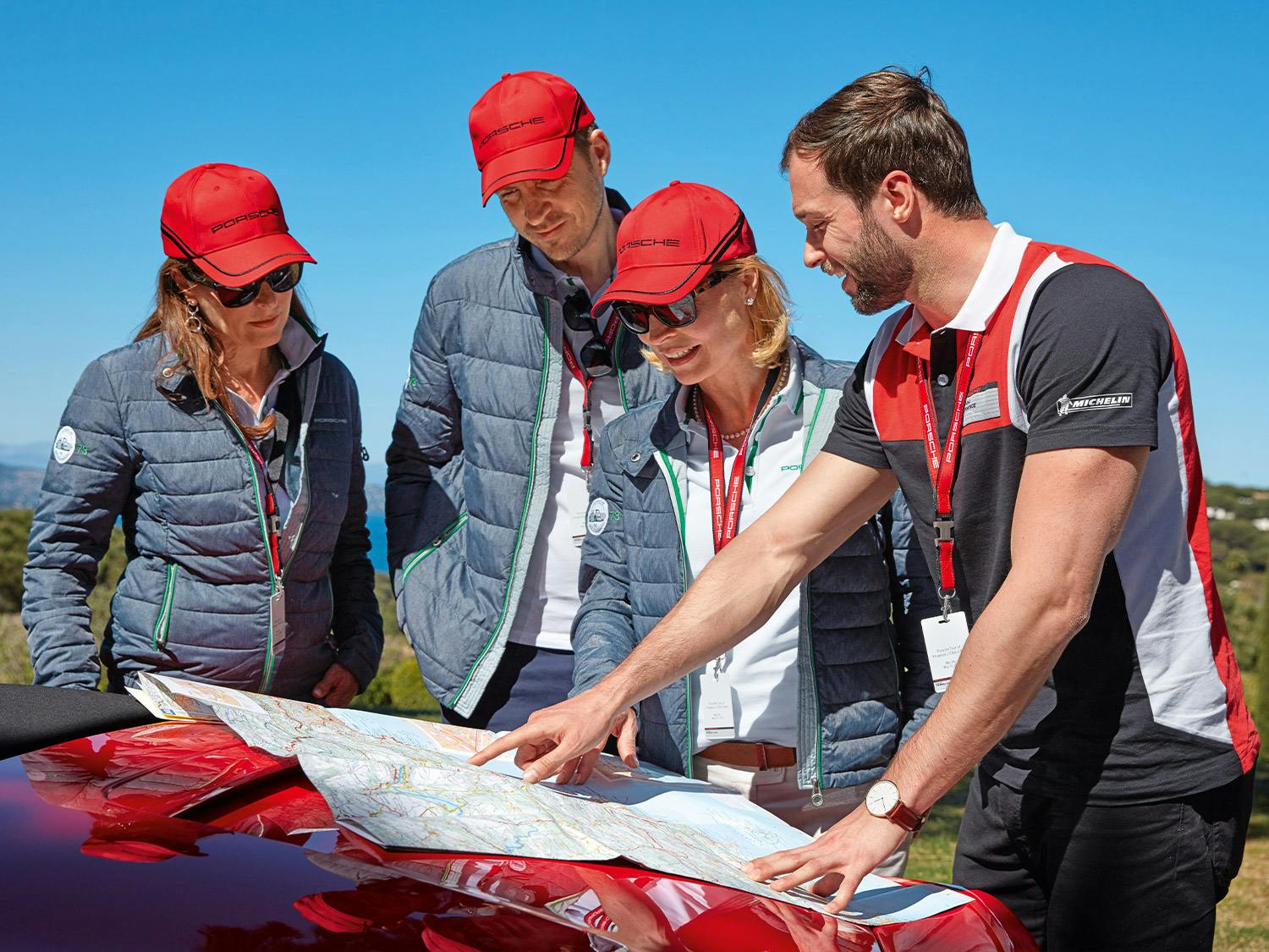 A group of people with red Porsche caps looking at a map.