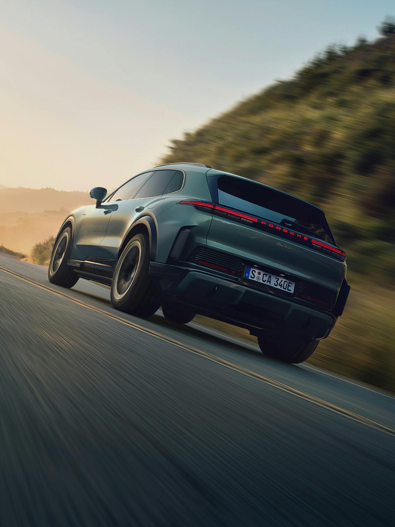 Rear view of the new Porsche Cayenne E4 speeding along a winding road at sunset with motion blur and glowing LED taillights.