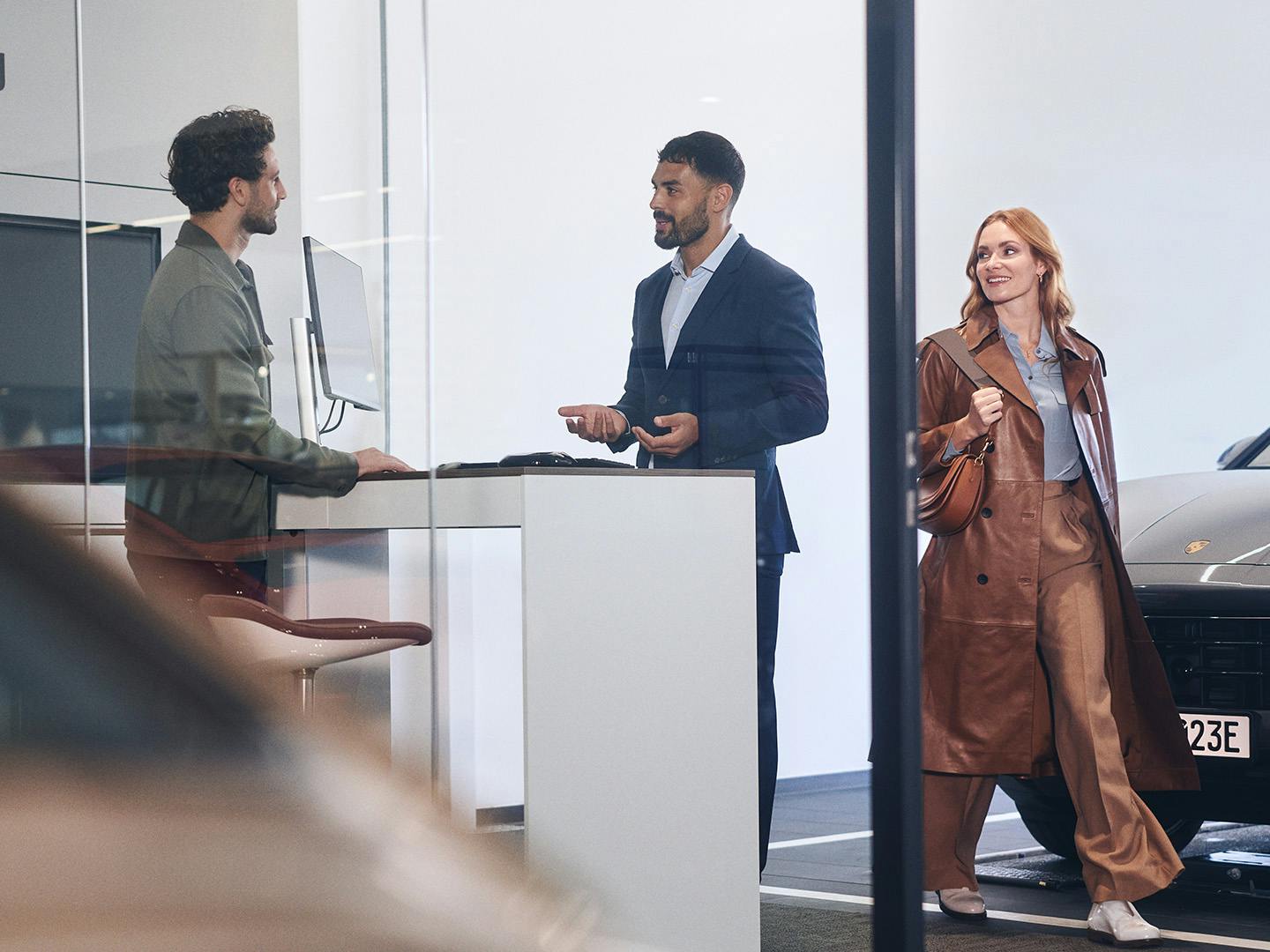 Deux hommes discutent à la réception d’un Centre (Service) Porsche. Une femme passe en arrière-plan.