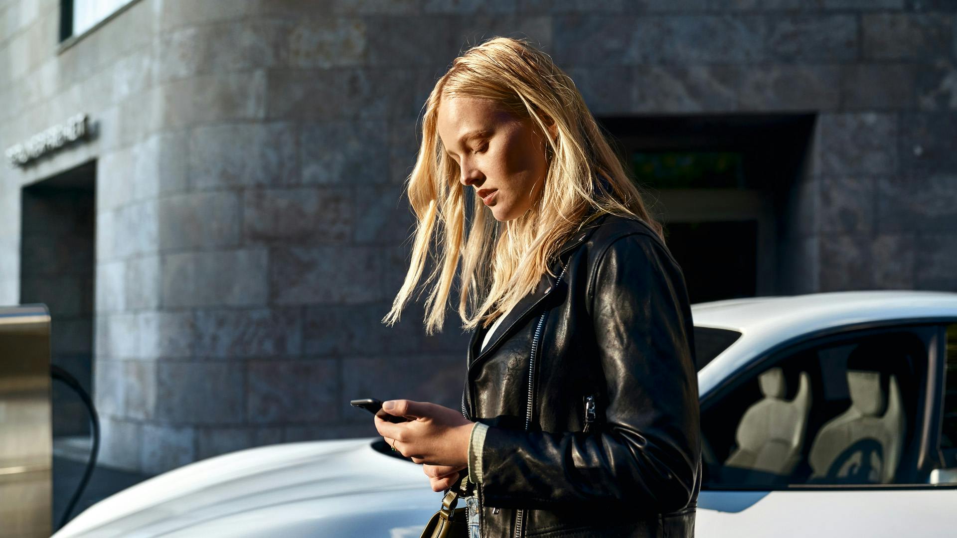 A lady using her mobile phone to interact with her Porsche.