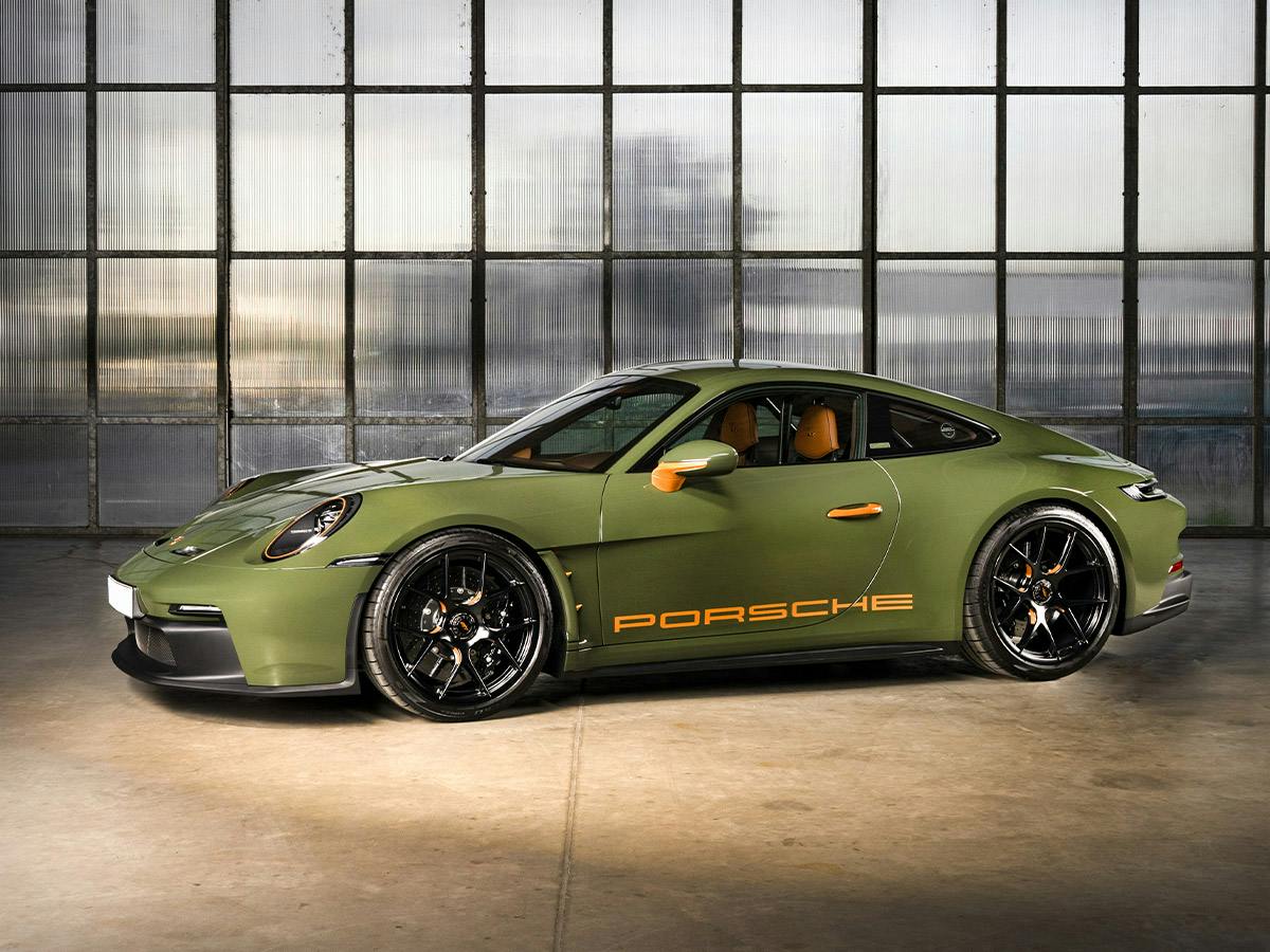 Side view of a Porsche 911 S/T in Paint to Sample colour Natoolive with Bahamayellow accents, parked indoors with large industrial windows in the background.