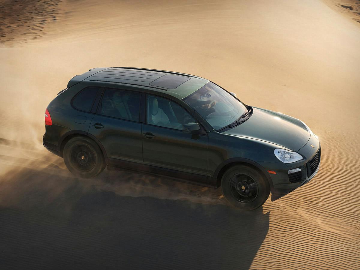 Bird’s‑eye view of the 1st Sonderwunsch Cayenne GTS in Blackolive driving up a sandy dune landscape.