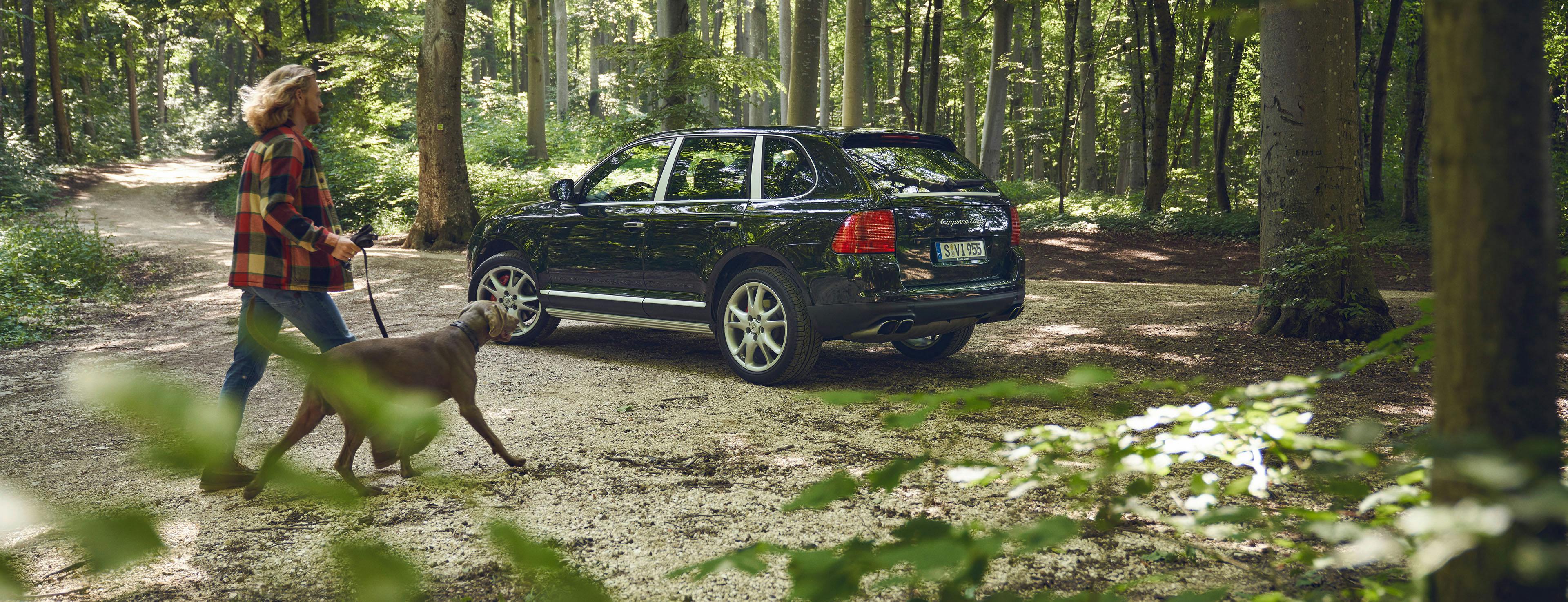 Porsche Cayenne parkt im Wald, Mann mit Hund.