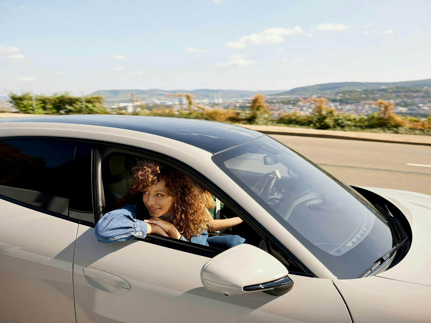Woman smiling in a Taycan Turbo S Cross Turismo with city view in background.