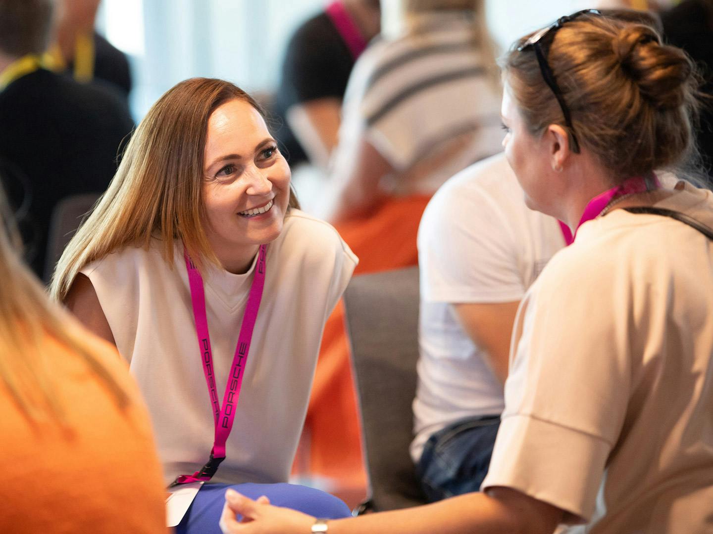 At a Porsche event, two cheerful young women are chatting with other people sitting around them.