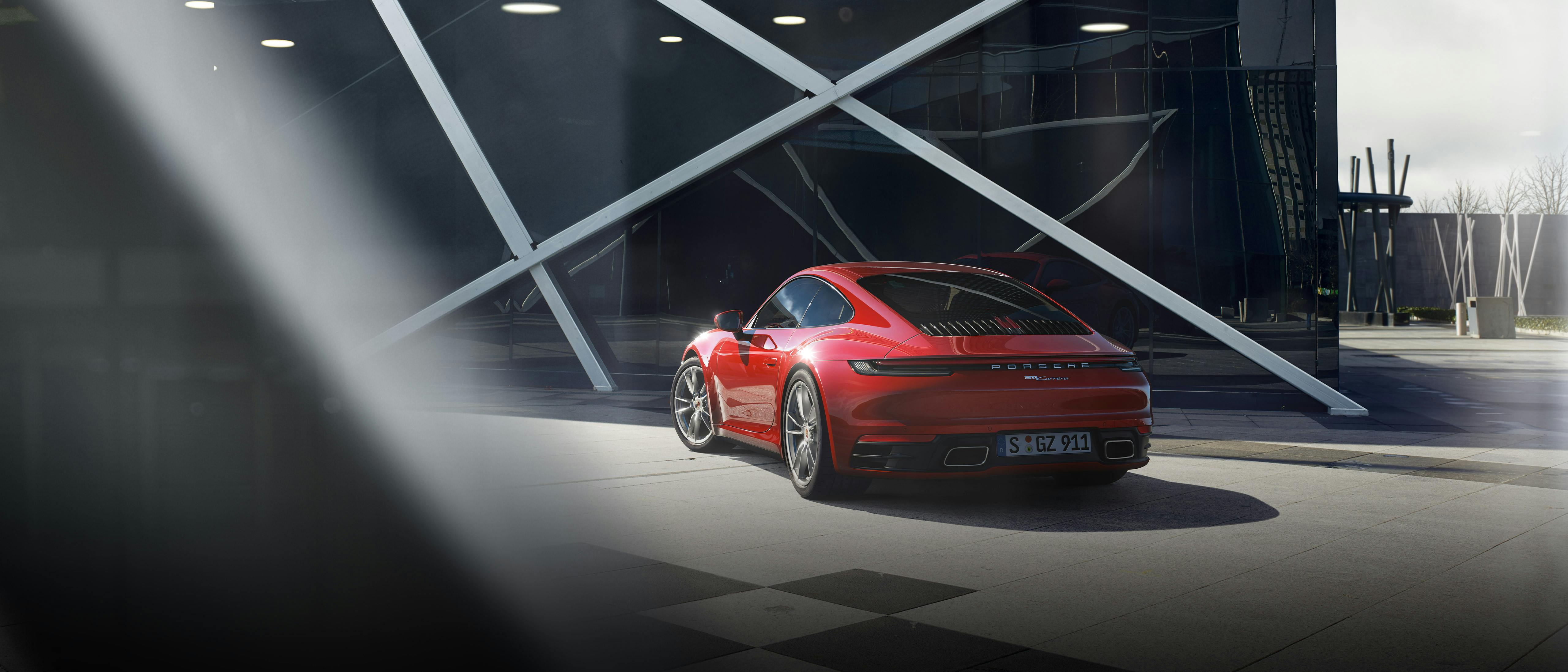 Une Porsche 911 Carrera rouge garée devant un impressionnant bâtiment moderne.