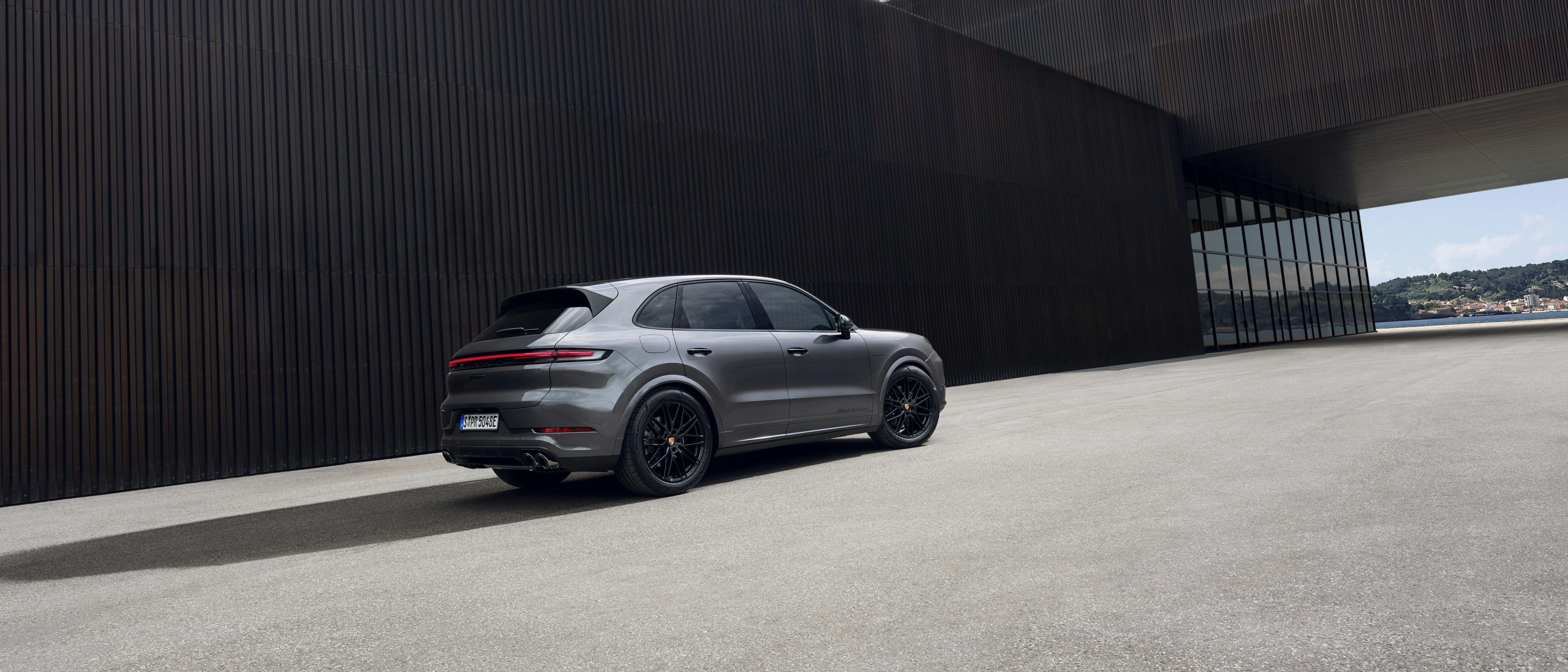 The Cayenne E-Hybrid Black Edition parked outside a modern building that is made up of dark textured material and also glass.