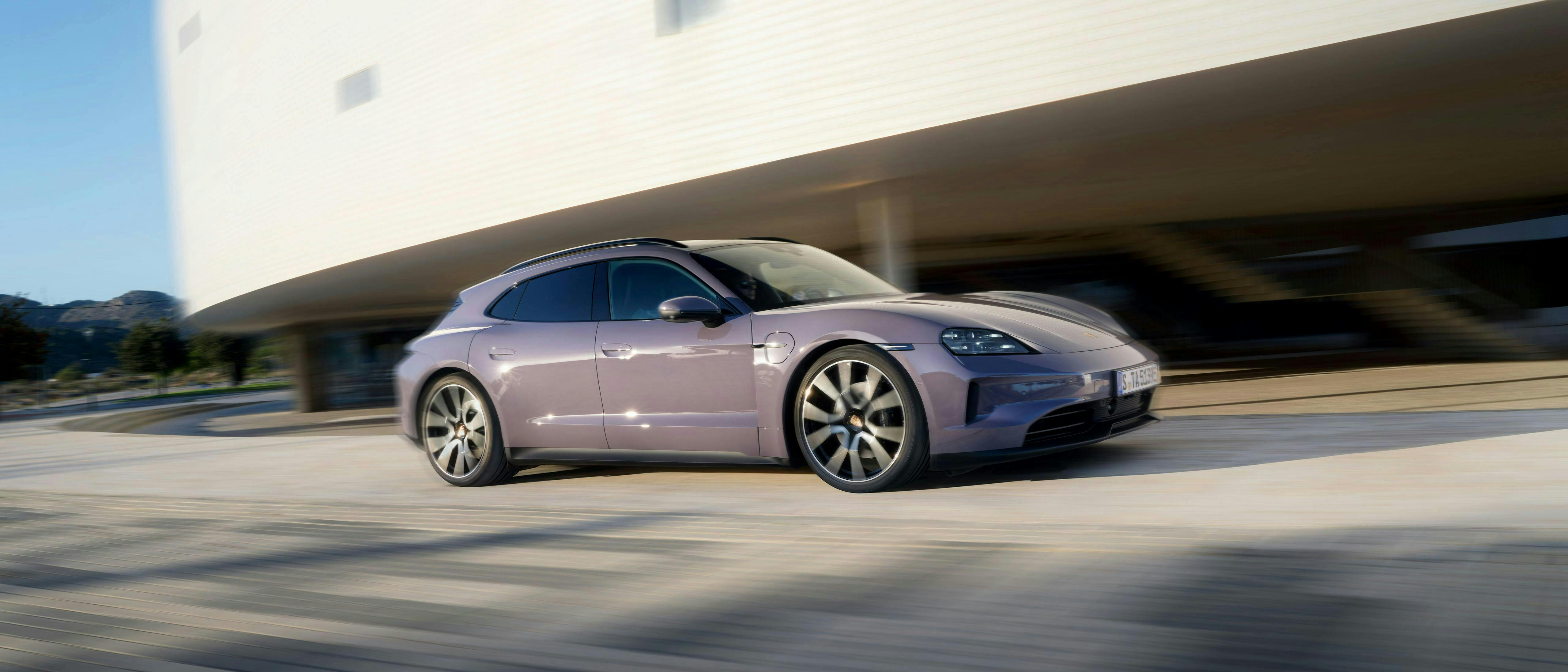 Een Porsche Taycan Sport Turismo rijdt langs een groot wit gebouw.