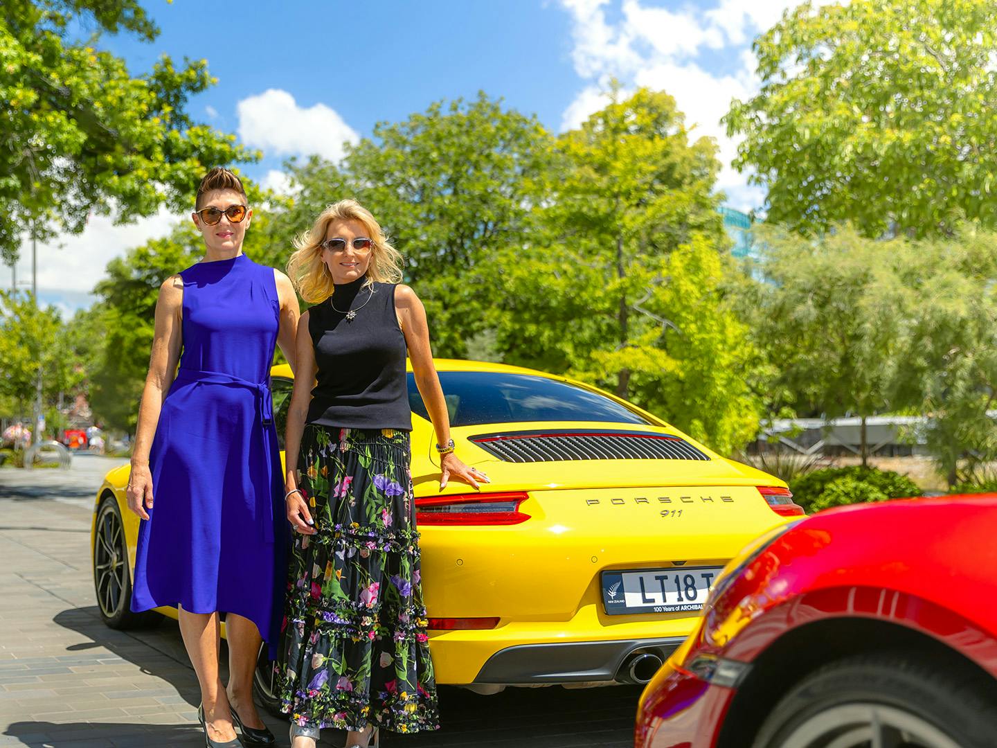 two women standing beside a yellow Porsche