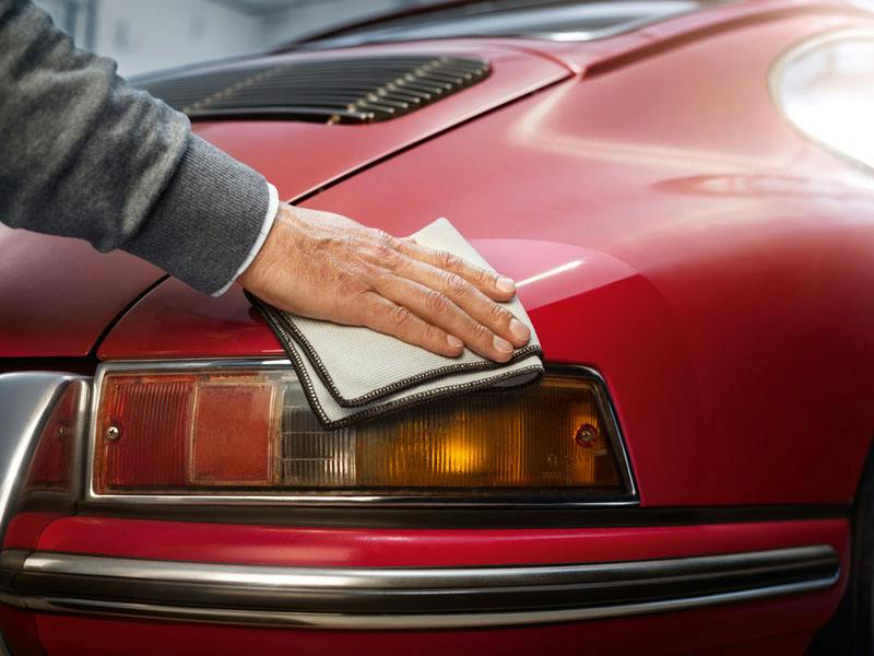 A man is cleaning his red Porsche 911 with a part of the Porsche Classic car care set.