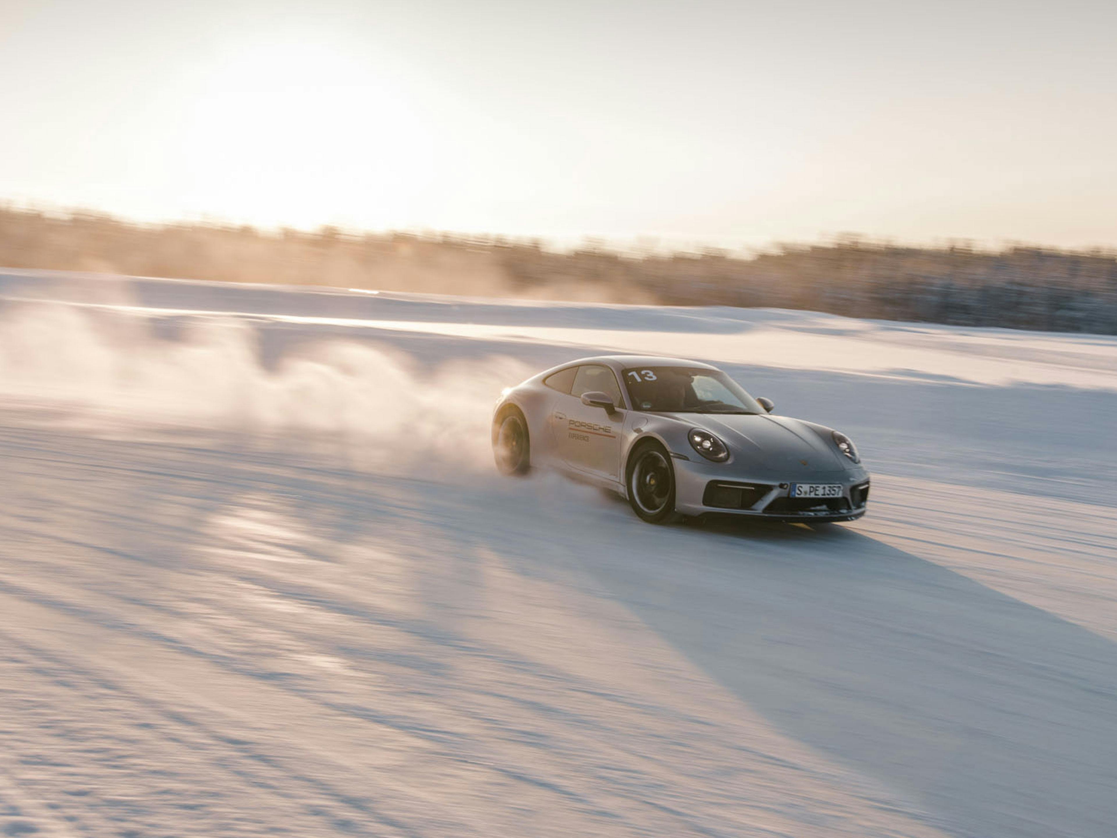 Silver Porsche 911 driving on a snow track at sunset
